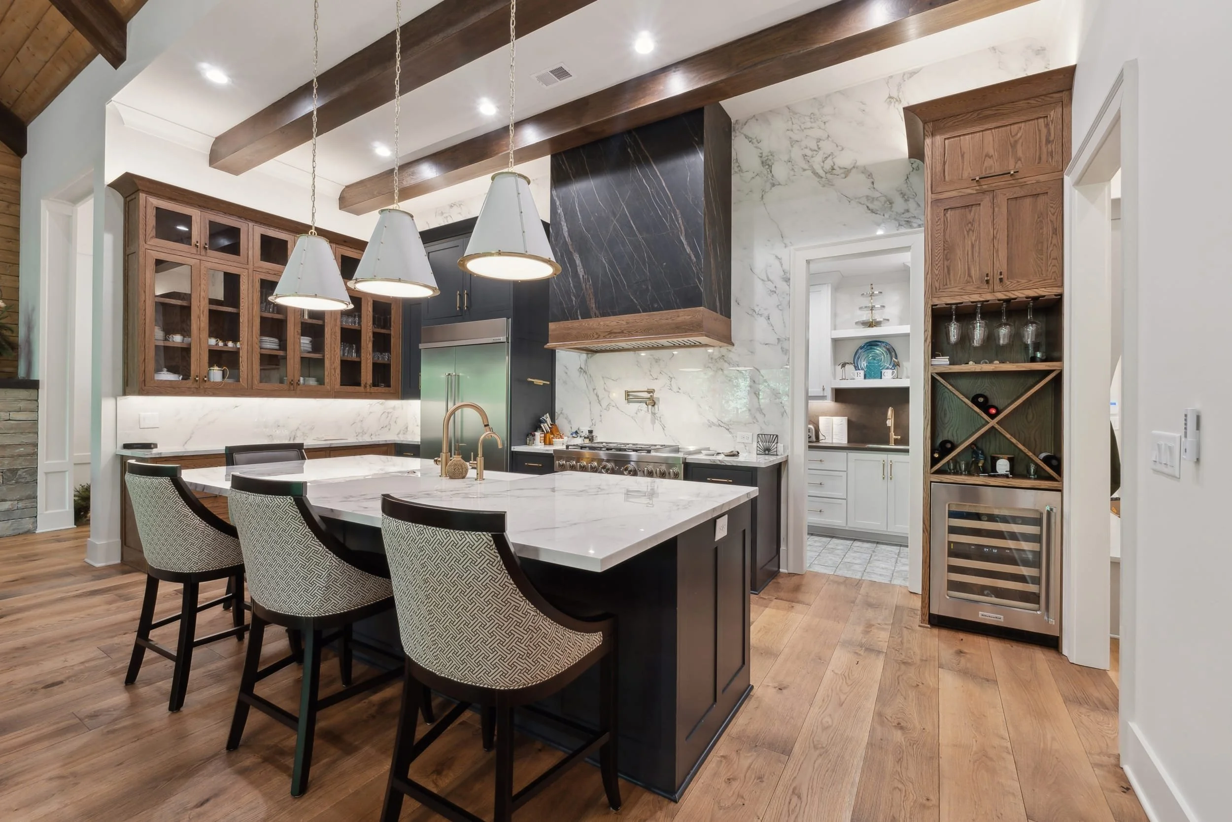 Modern kitchen with wooden ceiling beams, white and black cabinetry, a marble island, pendant lights, and a wine cooler.