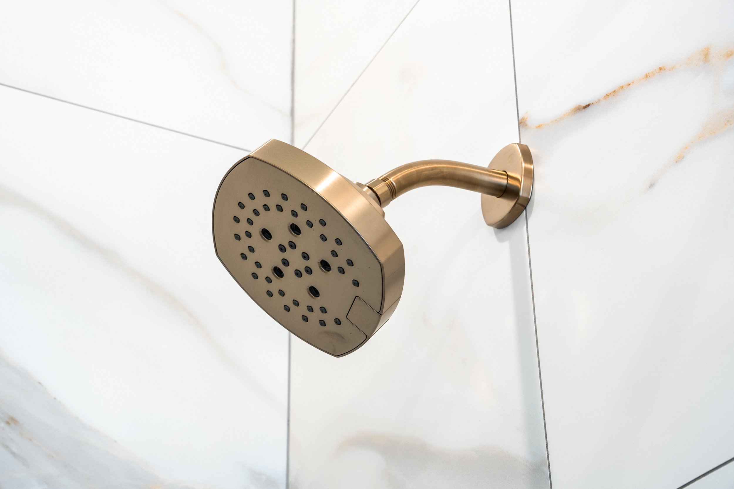 A modern showerhead attached to a white tiled wall in a bathroom.