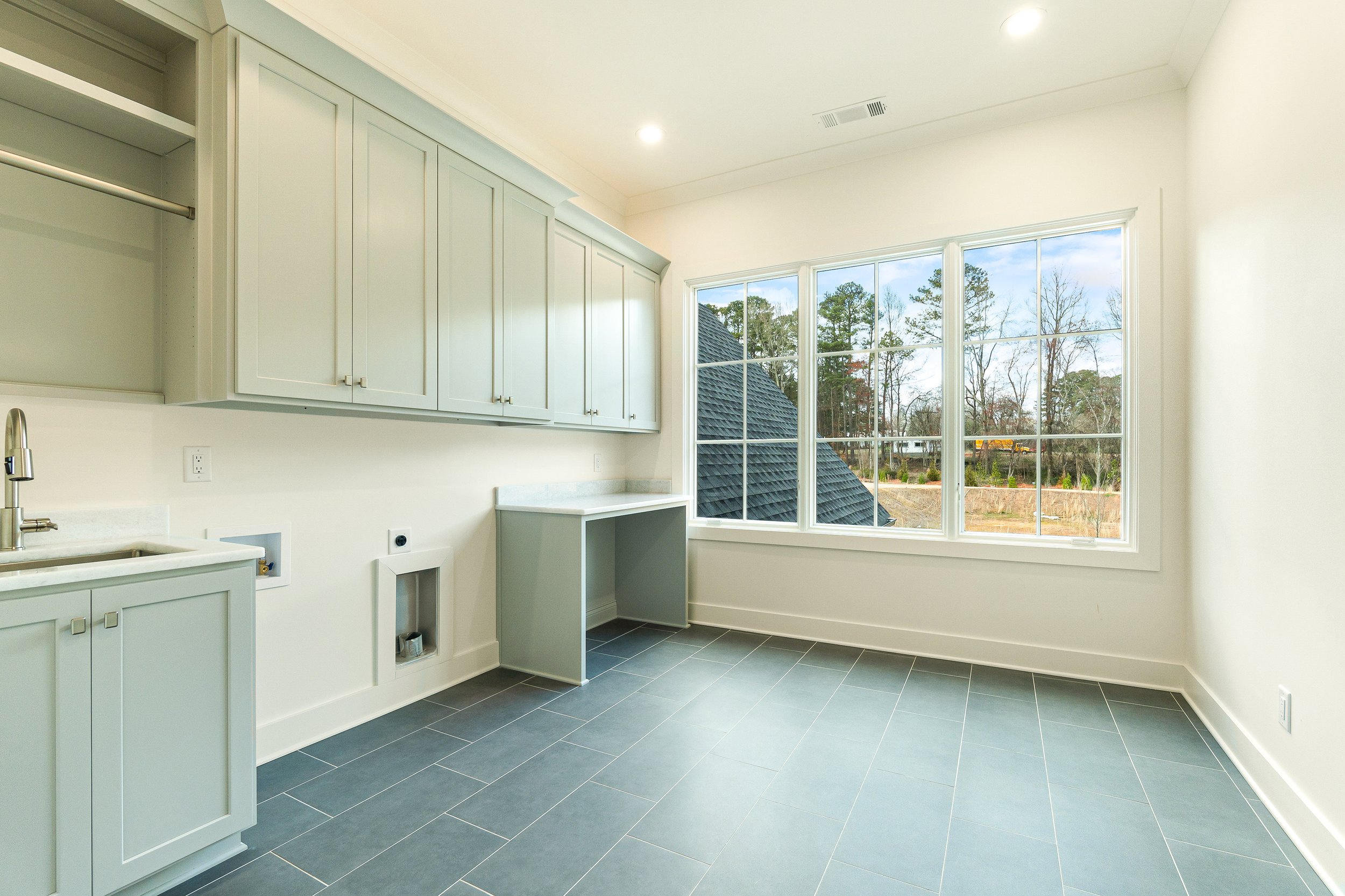 Bright, modern kitchen with white cabinetry and large window showing outdoor trees and a neighboring roof.