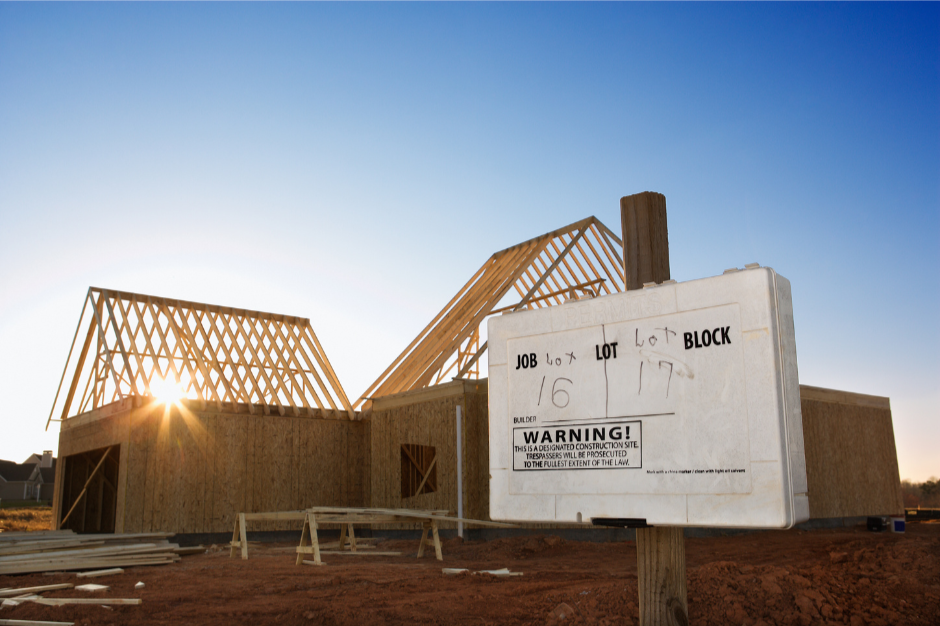 Construction site with a wooden house framework and a warning sign showing job lot and block numbers.
