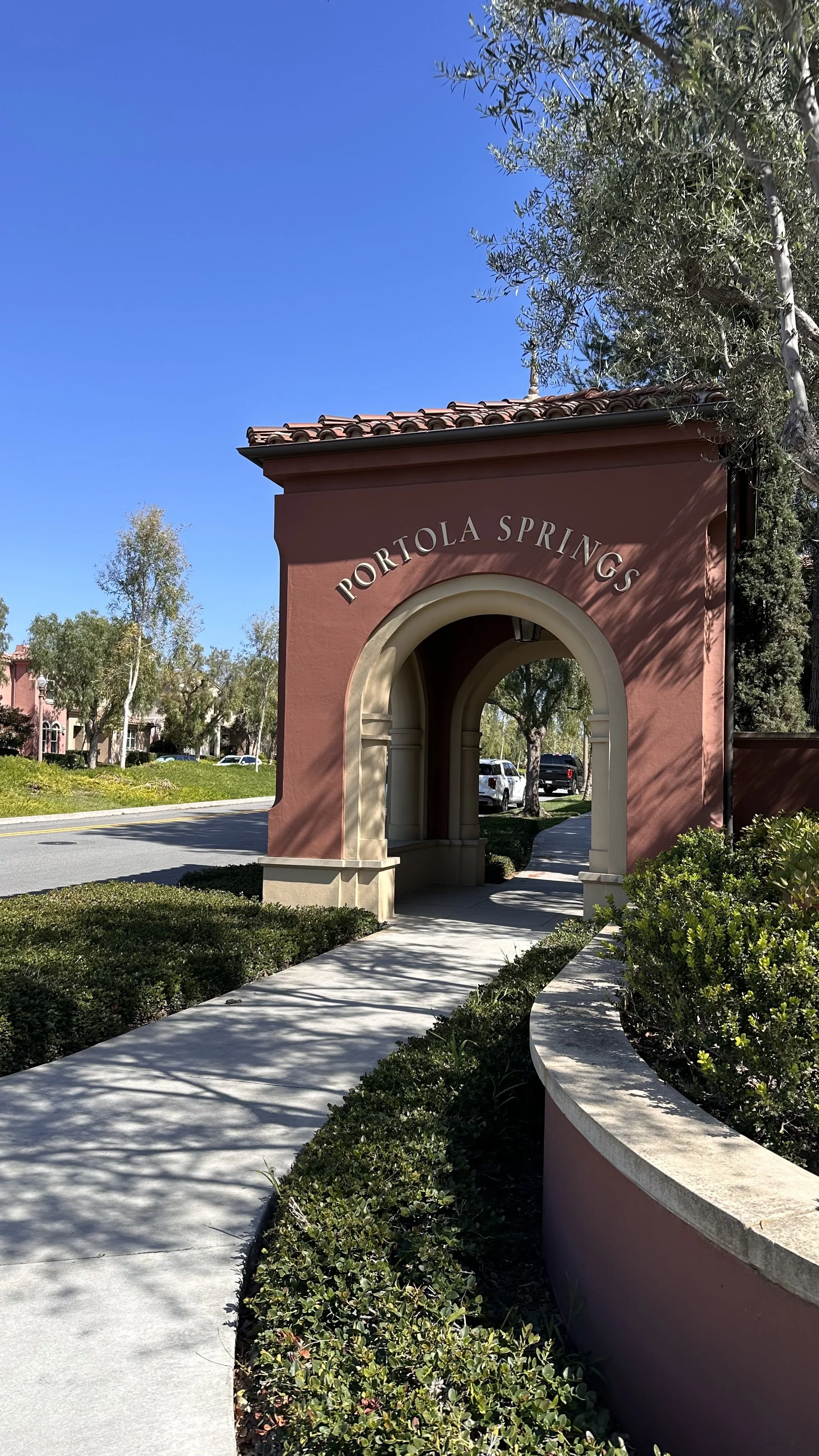 Entrance archway with the text "Portola Springs" on top, surrounded by greenery and trees, under a clear blue sky.