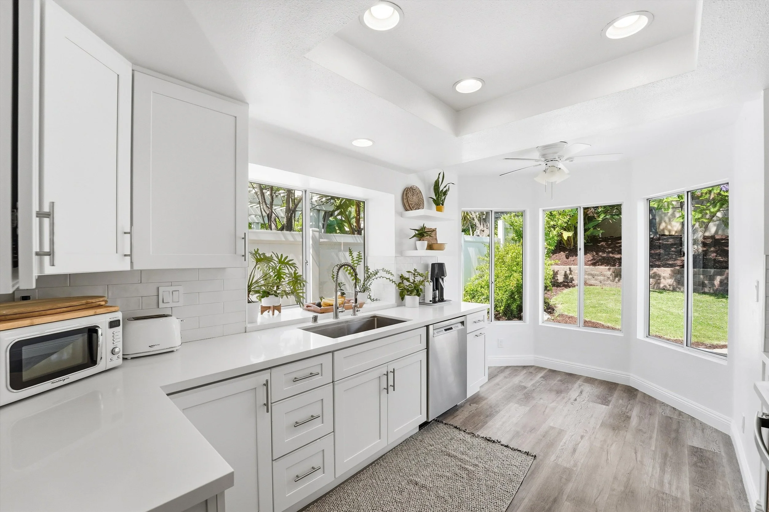 selling a home in irvine with a beautiful remodeled kitchen with white cabinets and lots of natural light. everything is white and there are a lot of windows