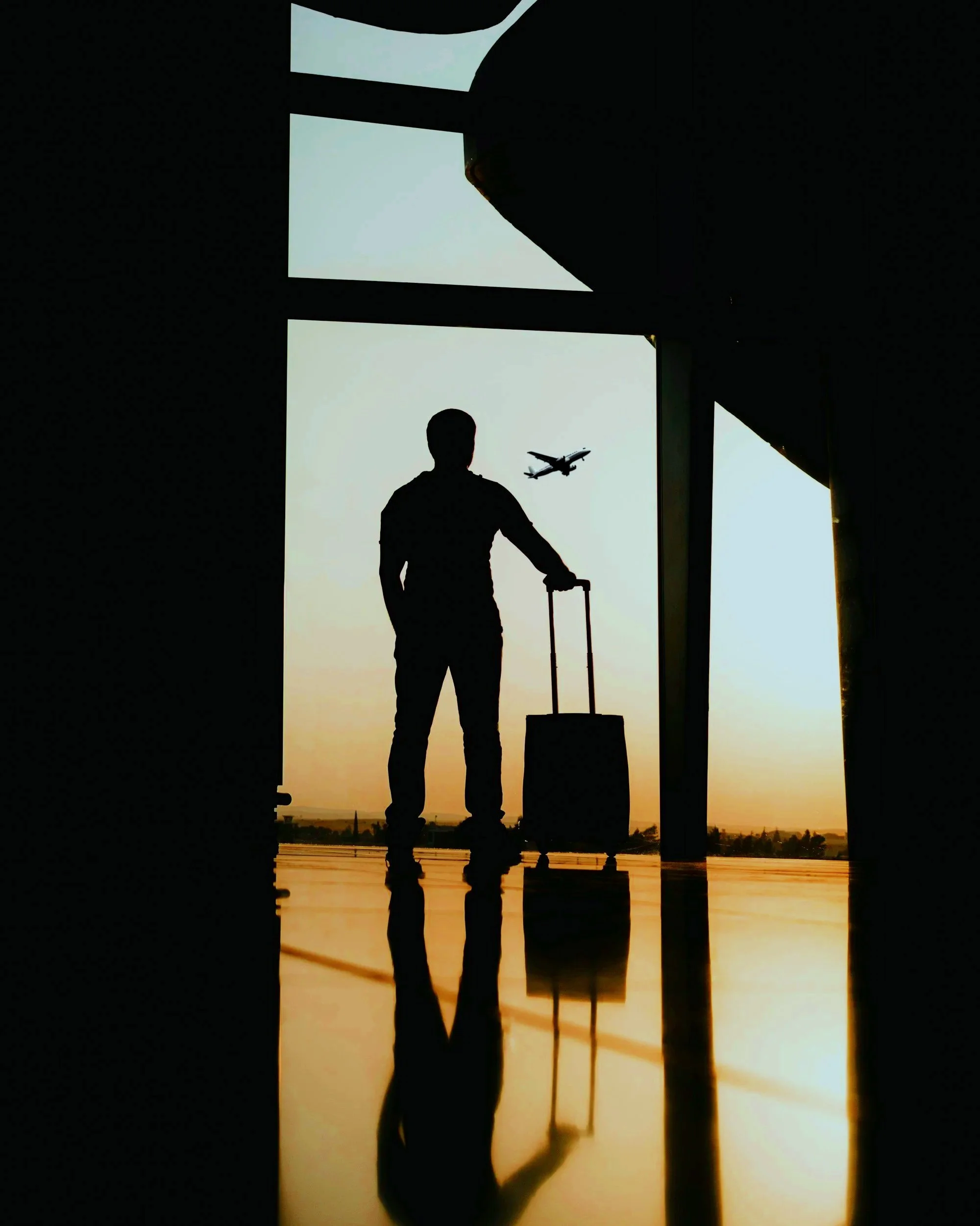 Silhouette de un hombre con maleta en un aeropuerto, vista de un atardecer con aviones en el cielo.
