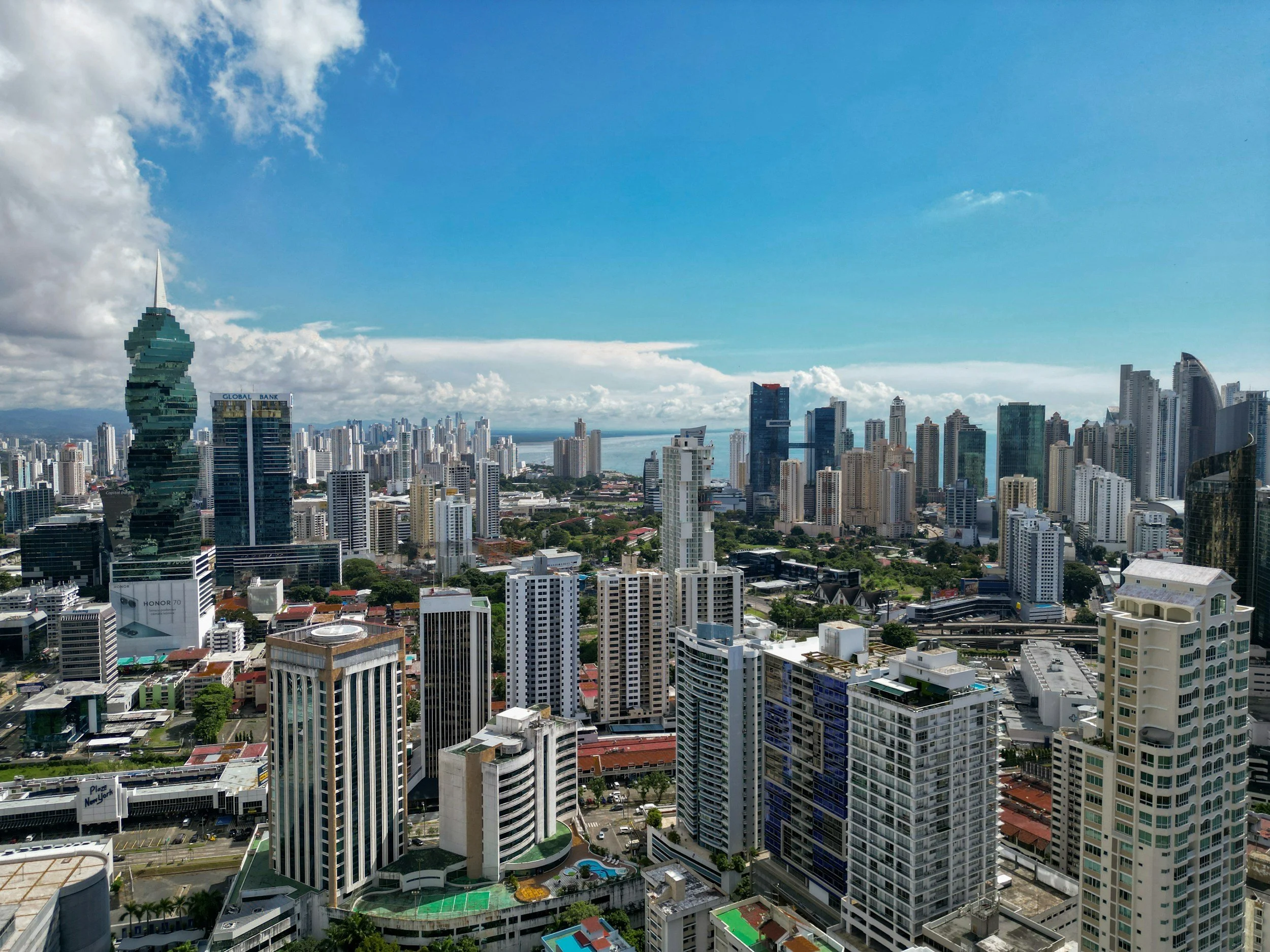 Vista panorámica de la ciudad con numerosos edificios altos y rascacielos, cielo parcialmente nublado y al fondo el mar.