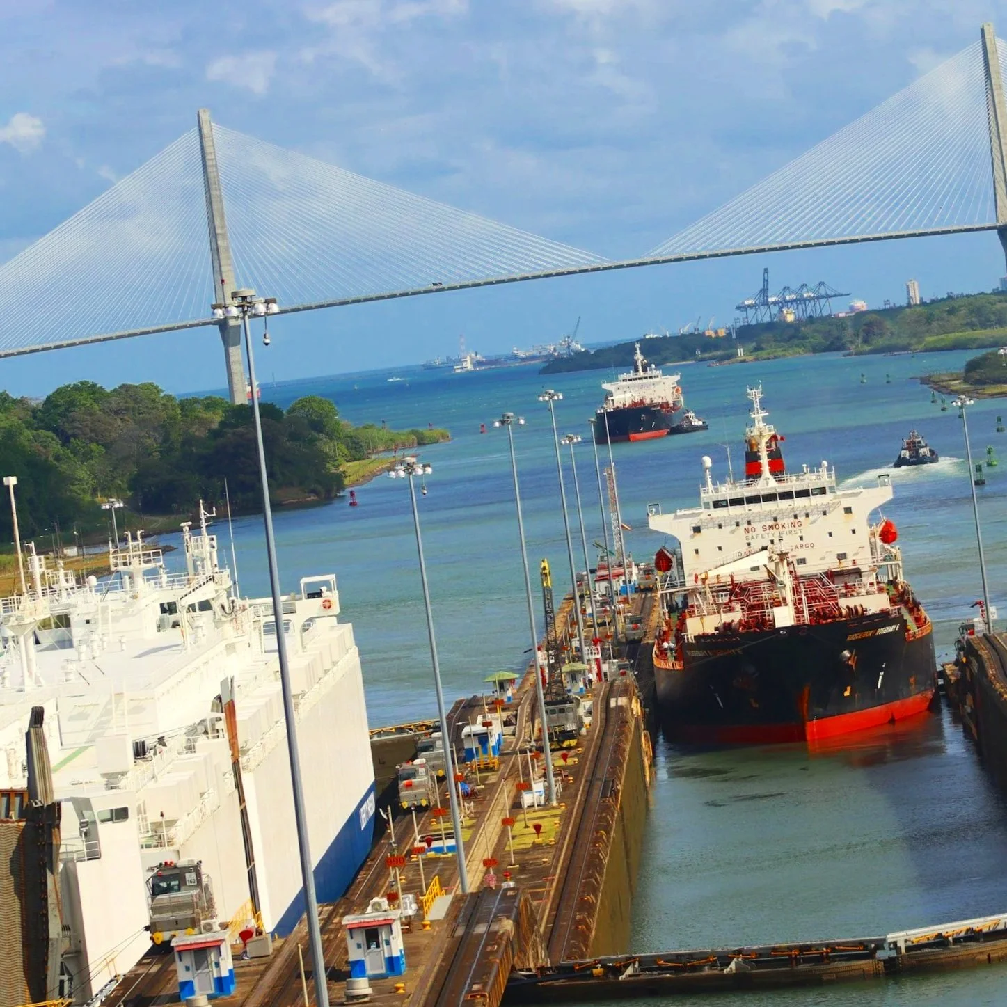 Vista de un puerto con barcos en la esclusa y un puente colgante en el fondo bajo un cielo azul con algunas nubes.