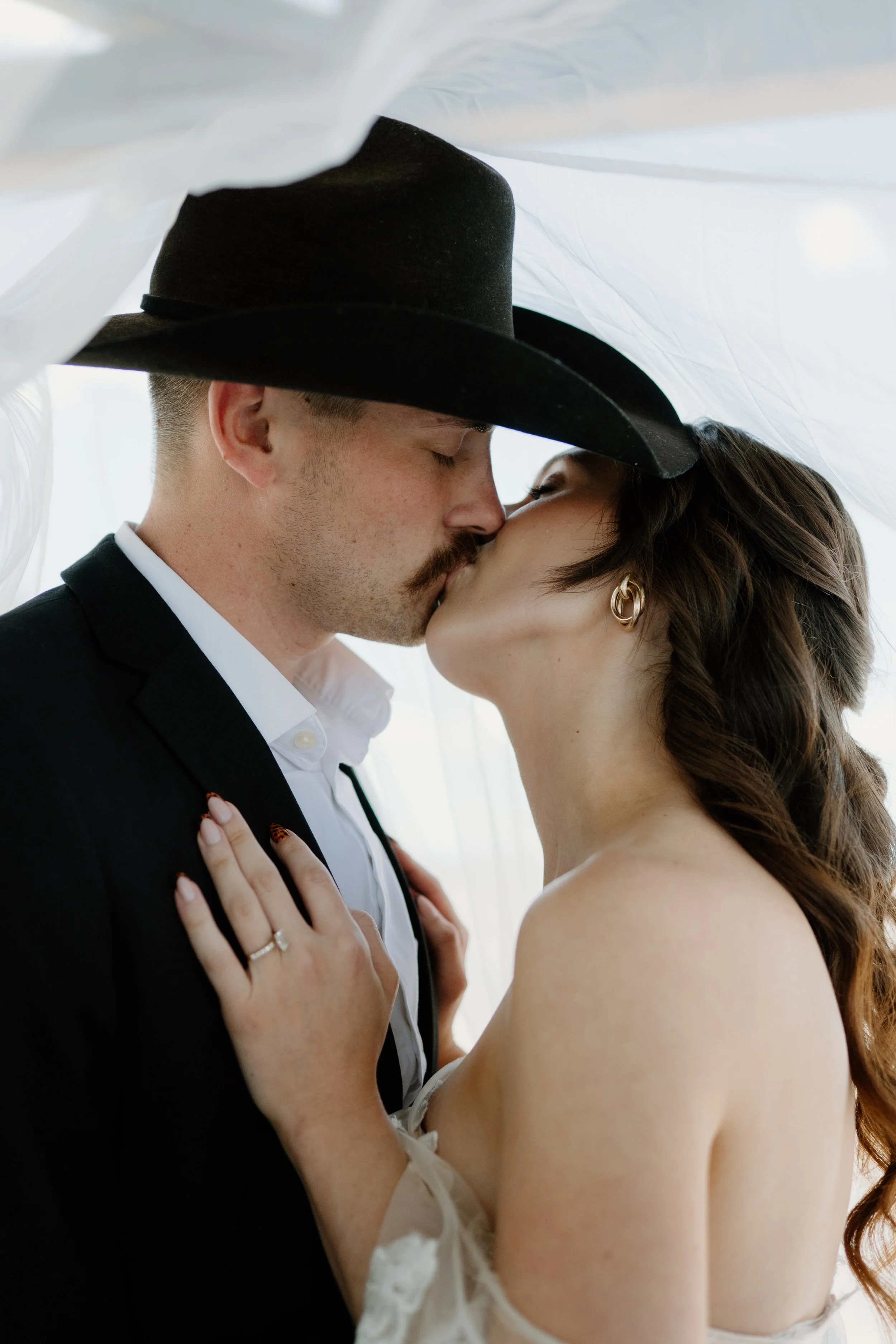 A married couple celebrating after their wedding ceremony with a kiss underneath their veil near Denver Colorado
