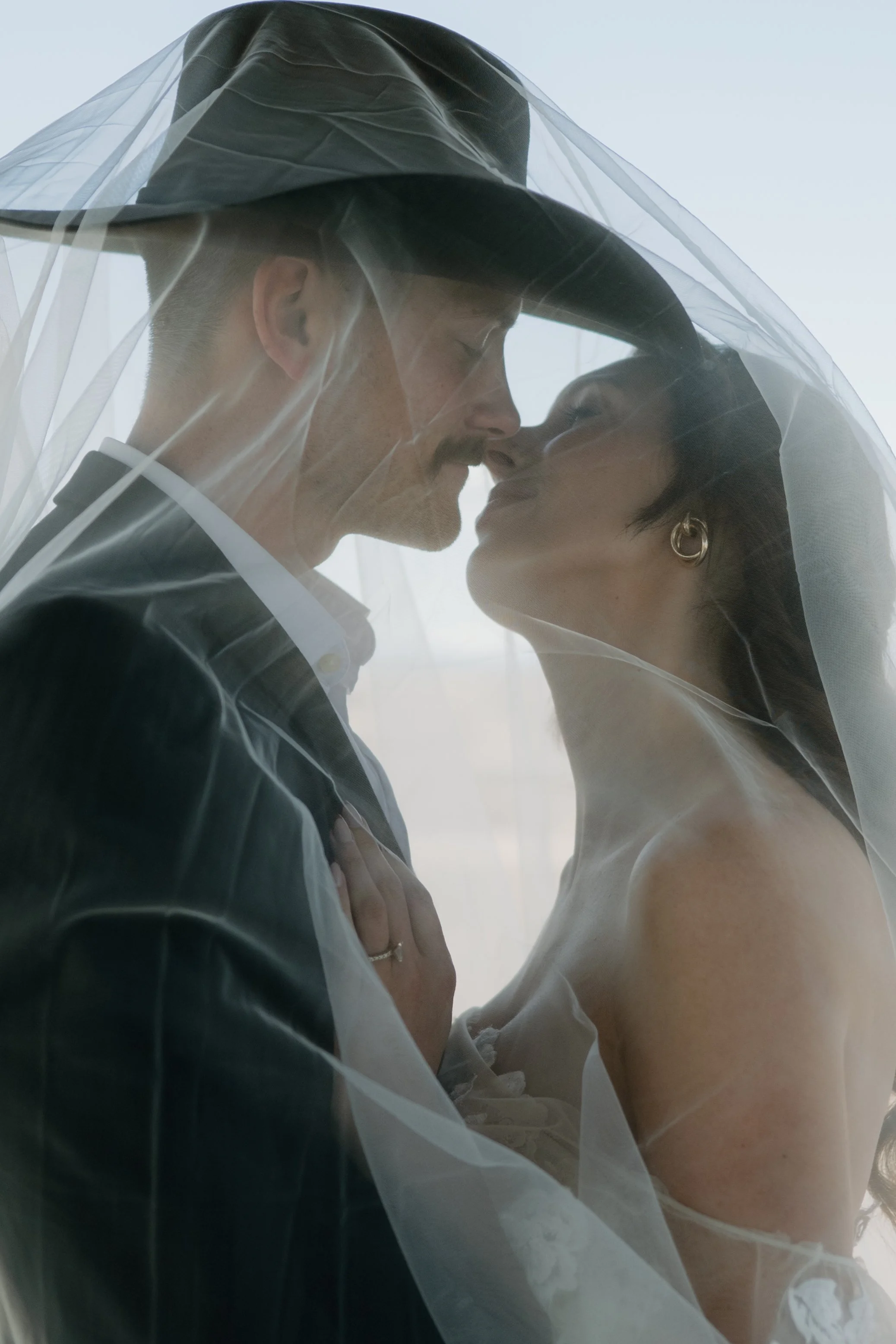 A western couple embracing underneath her veil wearing cowboy hats