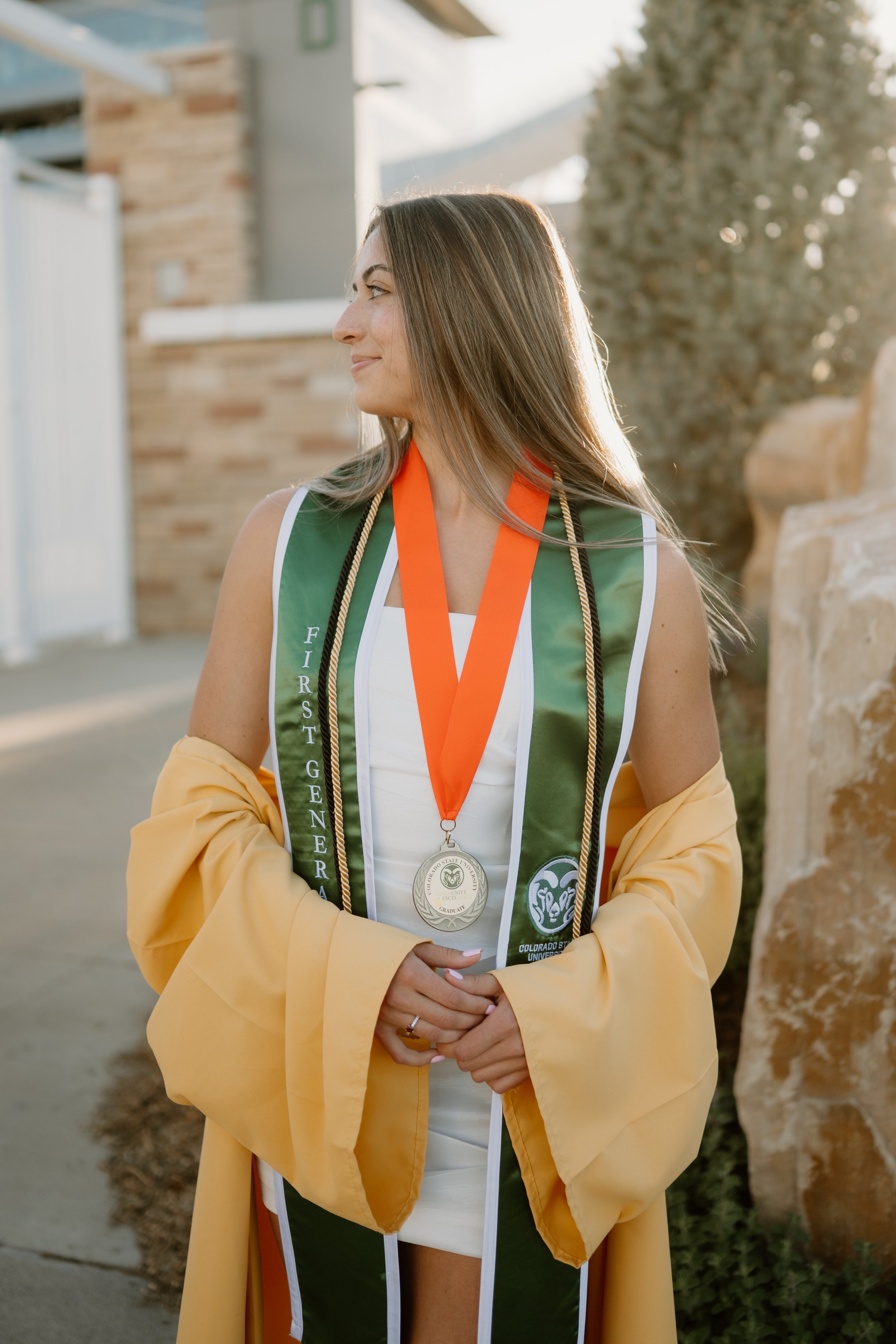 Colorado State University senior at Canvas Stadium in Fort Collins Colorado celebrating graduation with a gold gown and green CSU stole and cords at golden hour