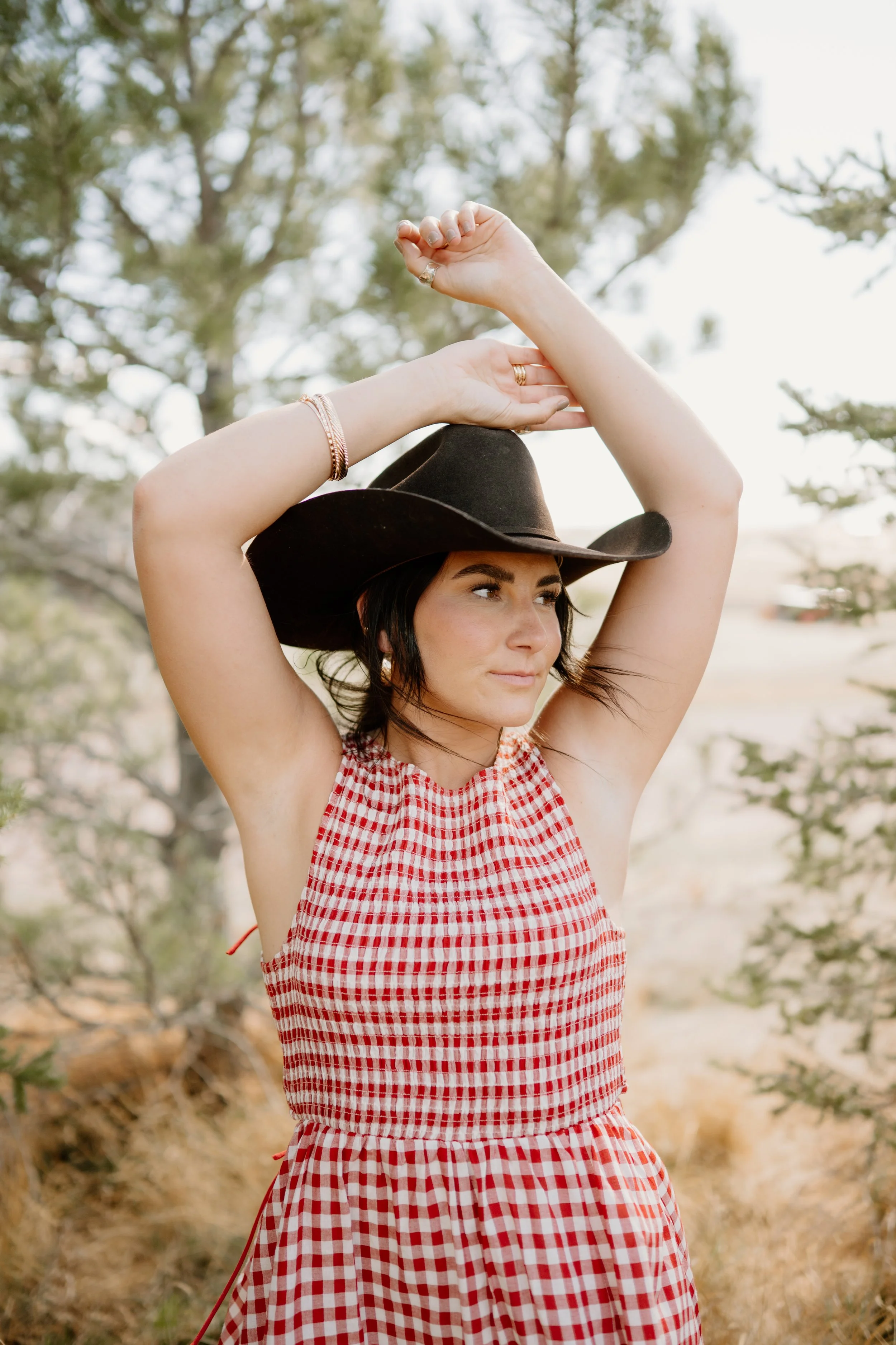 A woman holding her hands above her head, wearing a brown cowboy hat and a red and white checkered dress at Bonnie Blues Event Venue in Elizabeth Colorado