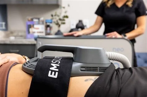 A person receiving a treatment or examination with a medical device labeled EMS on their lower abdomen, while a healthcare professional observes in a clinical setting.
