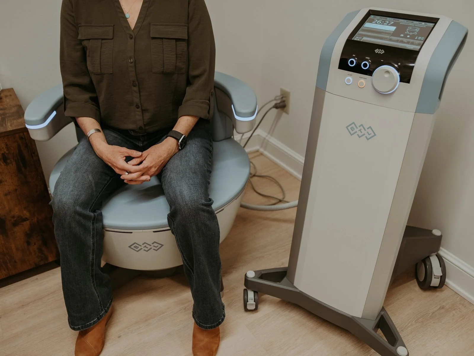 Patient seated fully clothed on the Emsella chair at Atlas