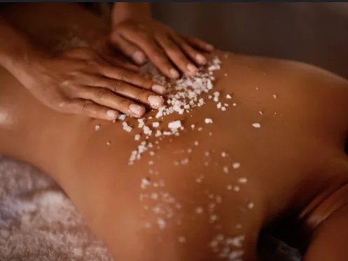 A person receiving a salt scrub massage on their back in a spa setting.