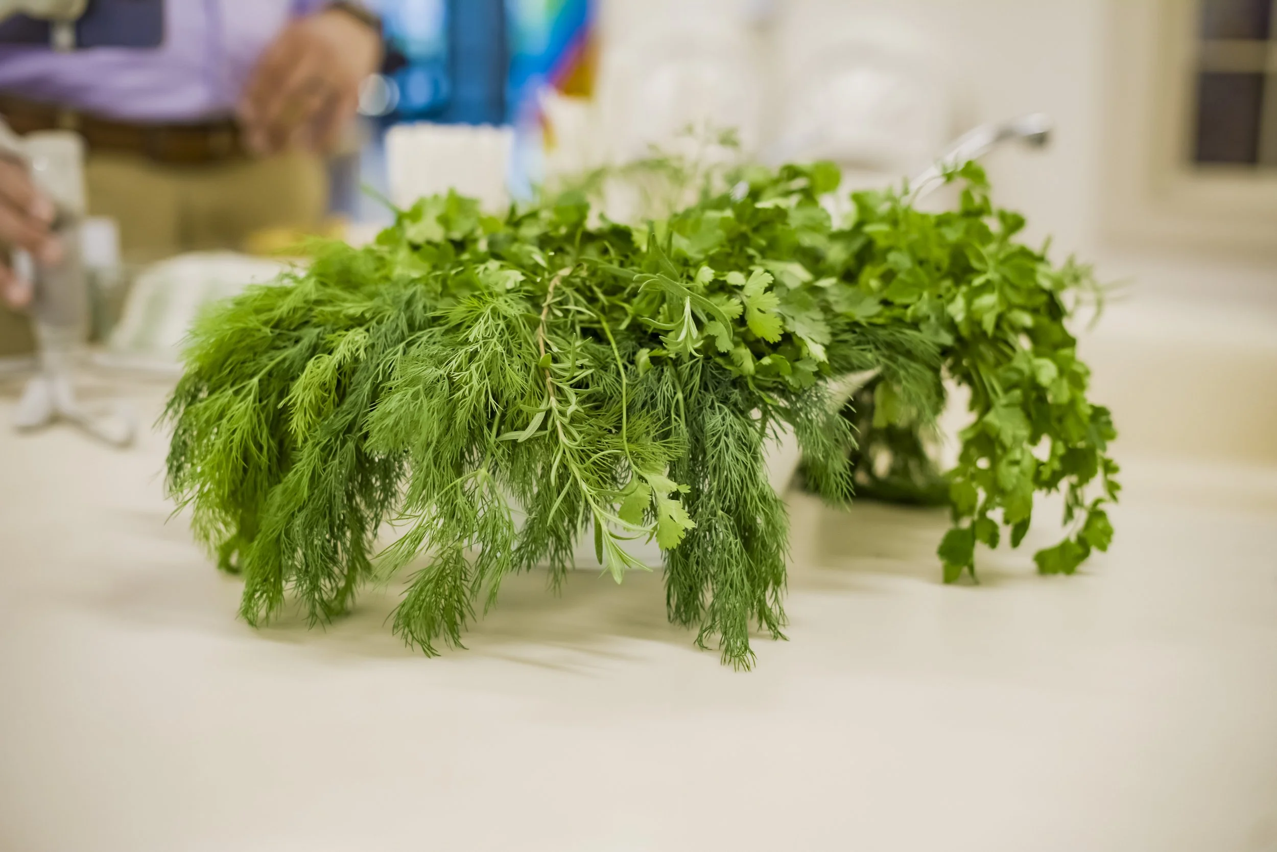 A bunch of fresh green herbs, including parsley, cilantro, and dill, arranged on a white surface in a kitchen setting.
