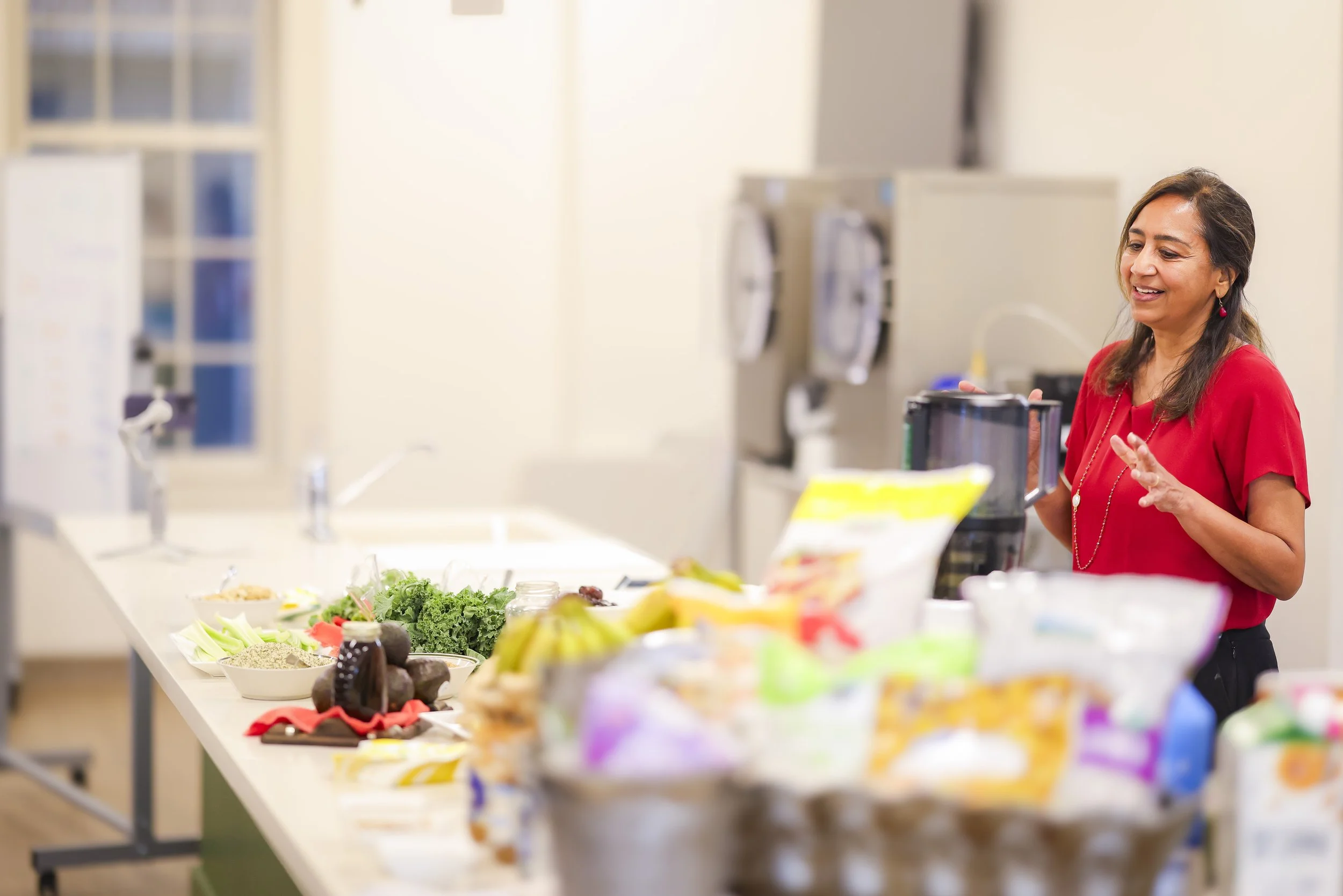 Smiling woman in red shirt standing at kitchen counter with groceries and food ingredients.