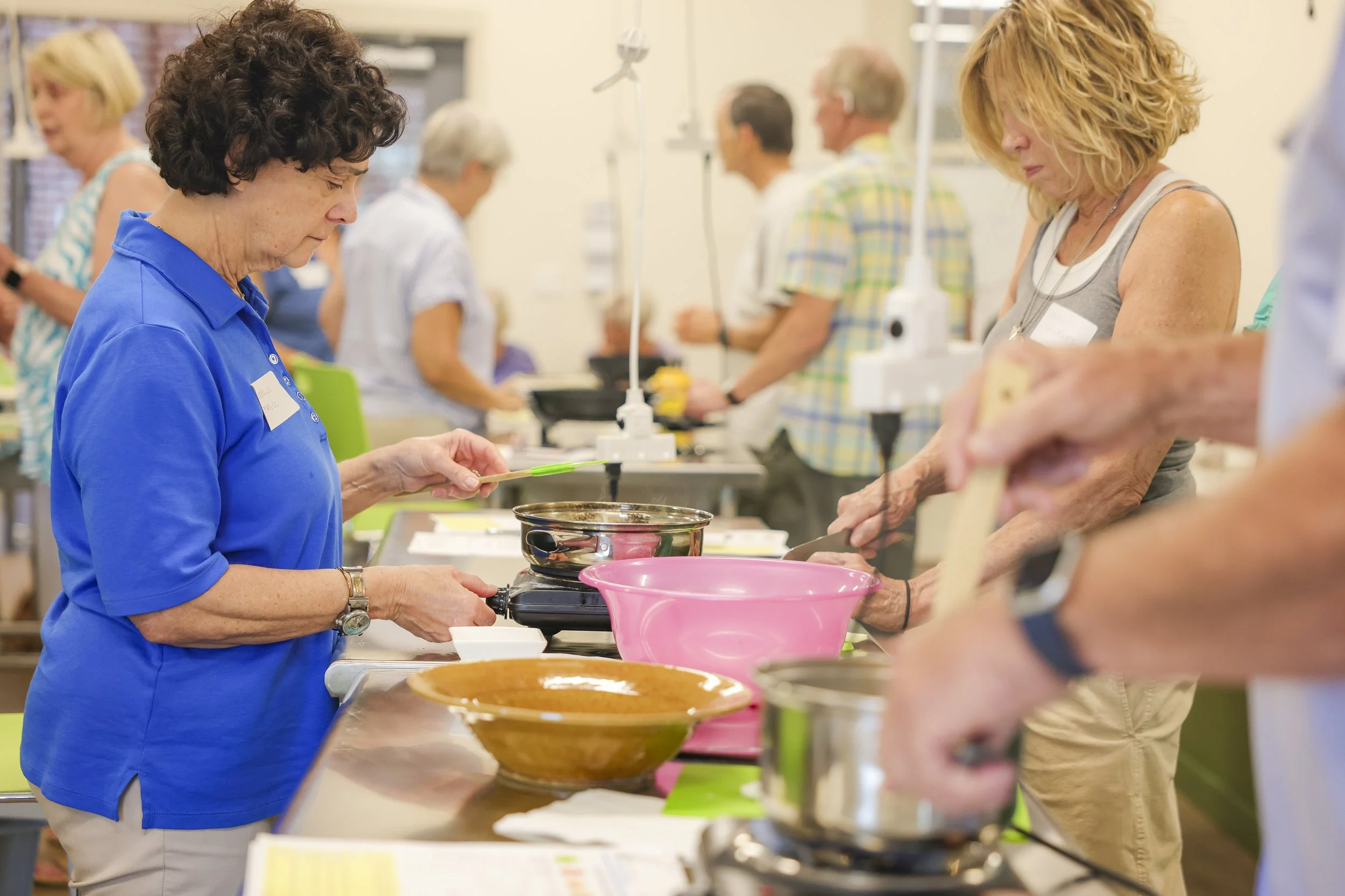 Several people participating in a cooking class, preparing food at a long table with various bowls and utensils.