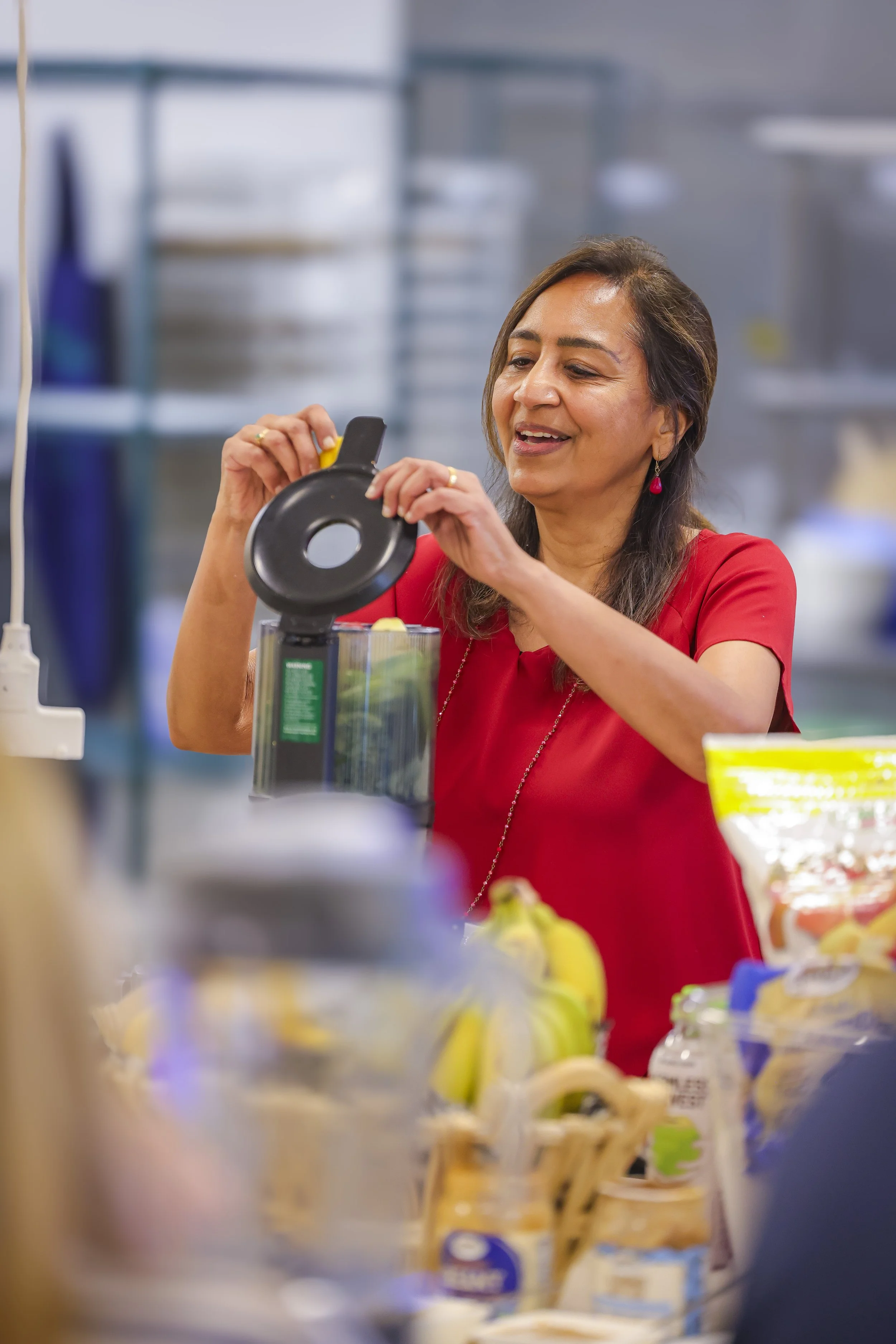 A woman wearing a red shirt in a grocery store, opening a container of food.