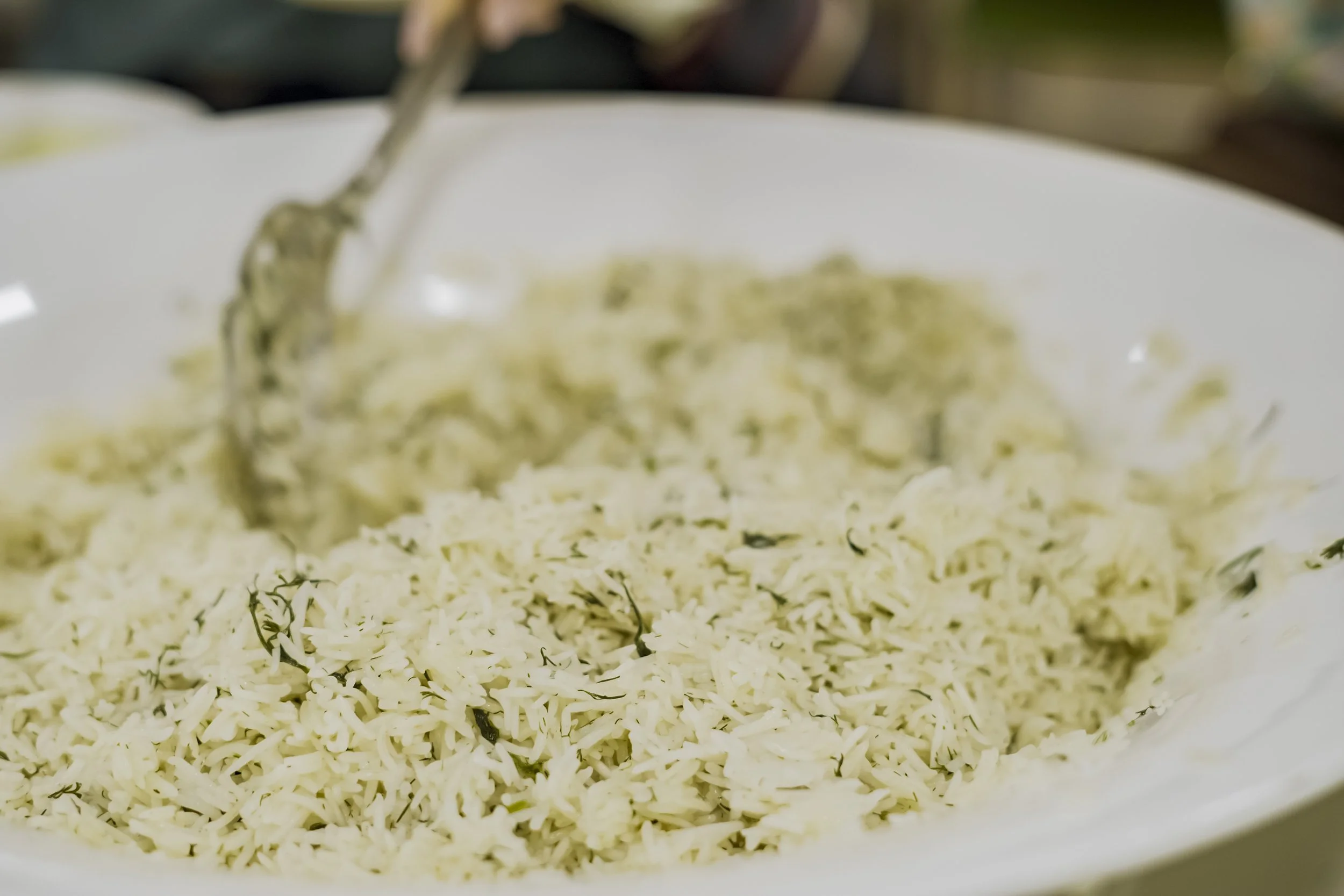 Close-up of rice with herbs in a white bowl with a spoon pouring more rice into the bowl.