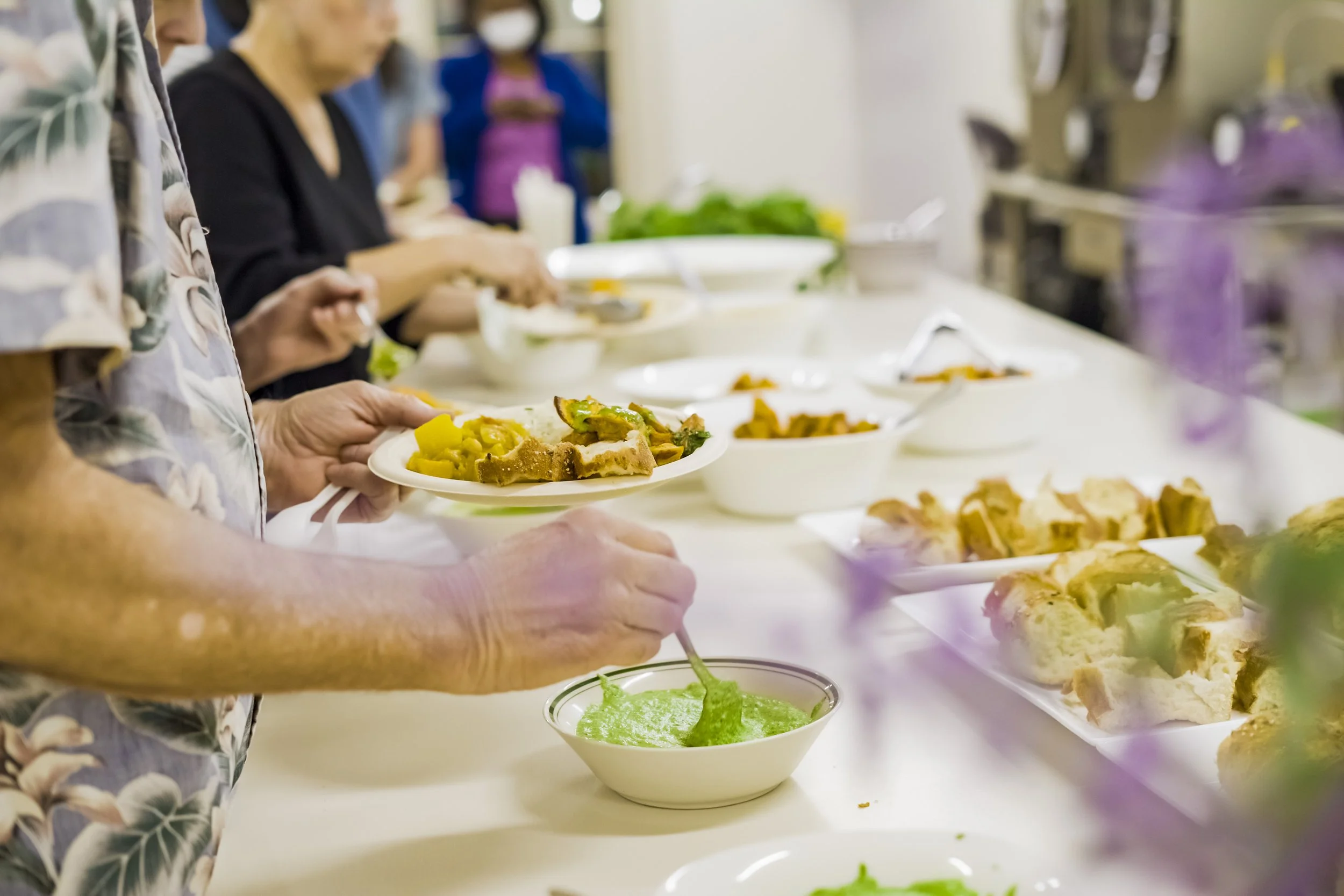 People serving themselves food at a buffet table with various dishes and bowls of soup.