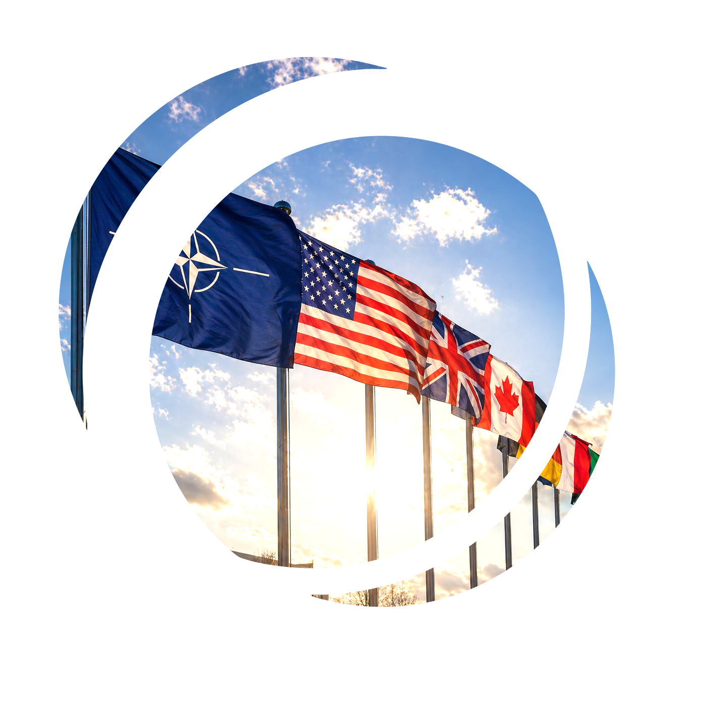 Multiple international flags, including the NATO emblem, American flag, British flag, Canadian flag, and others, flying on flagpoles against a sunset sky with scattered clouds.
