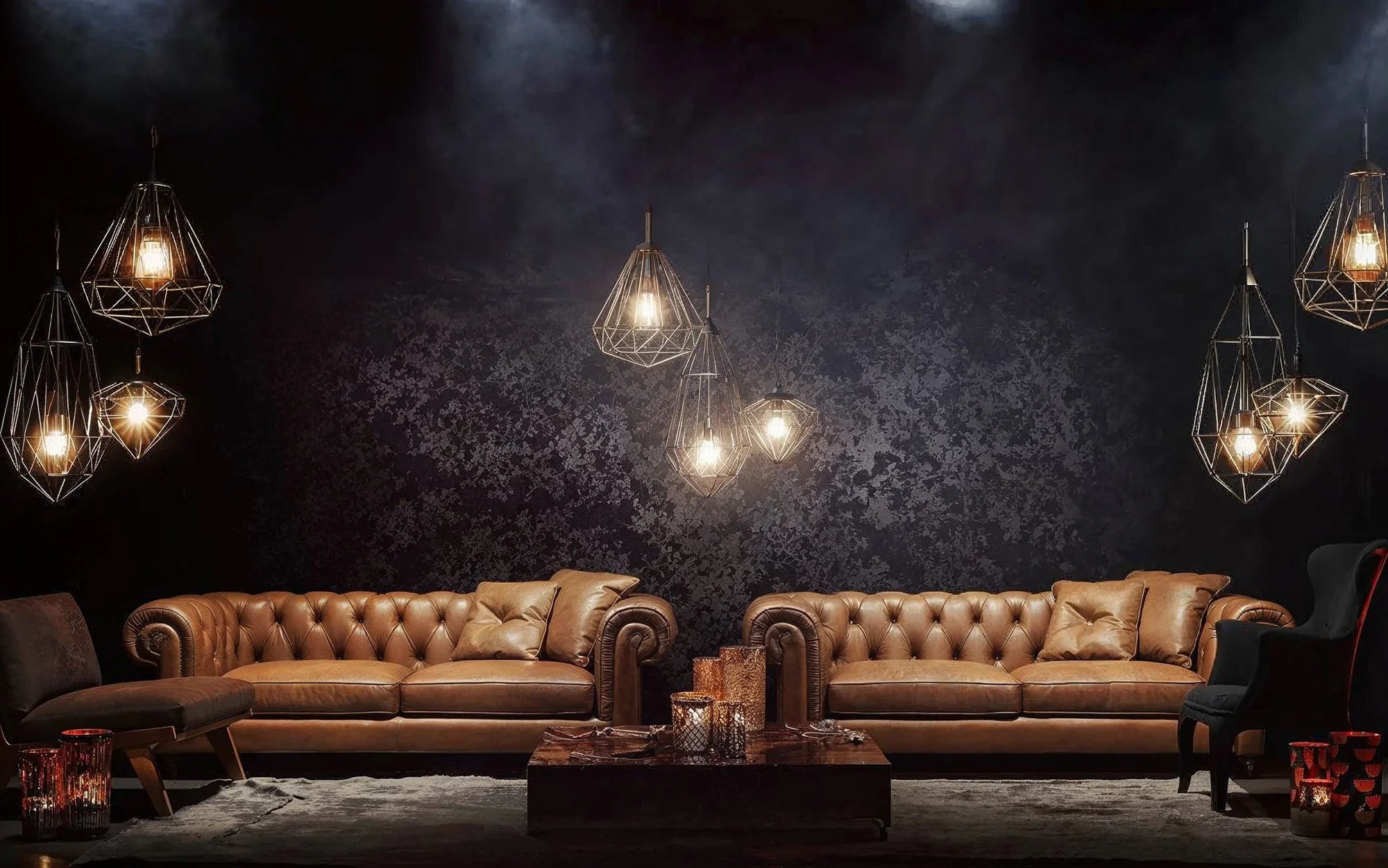 Living room with black wall, two brown leather sofas, one black wingback chair, modern pendant lights, candles on the coffee table, and a grey area rug.