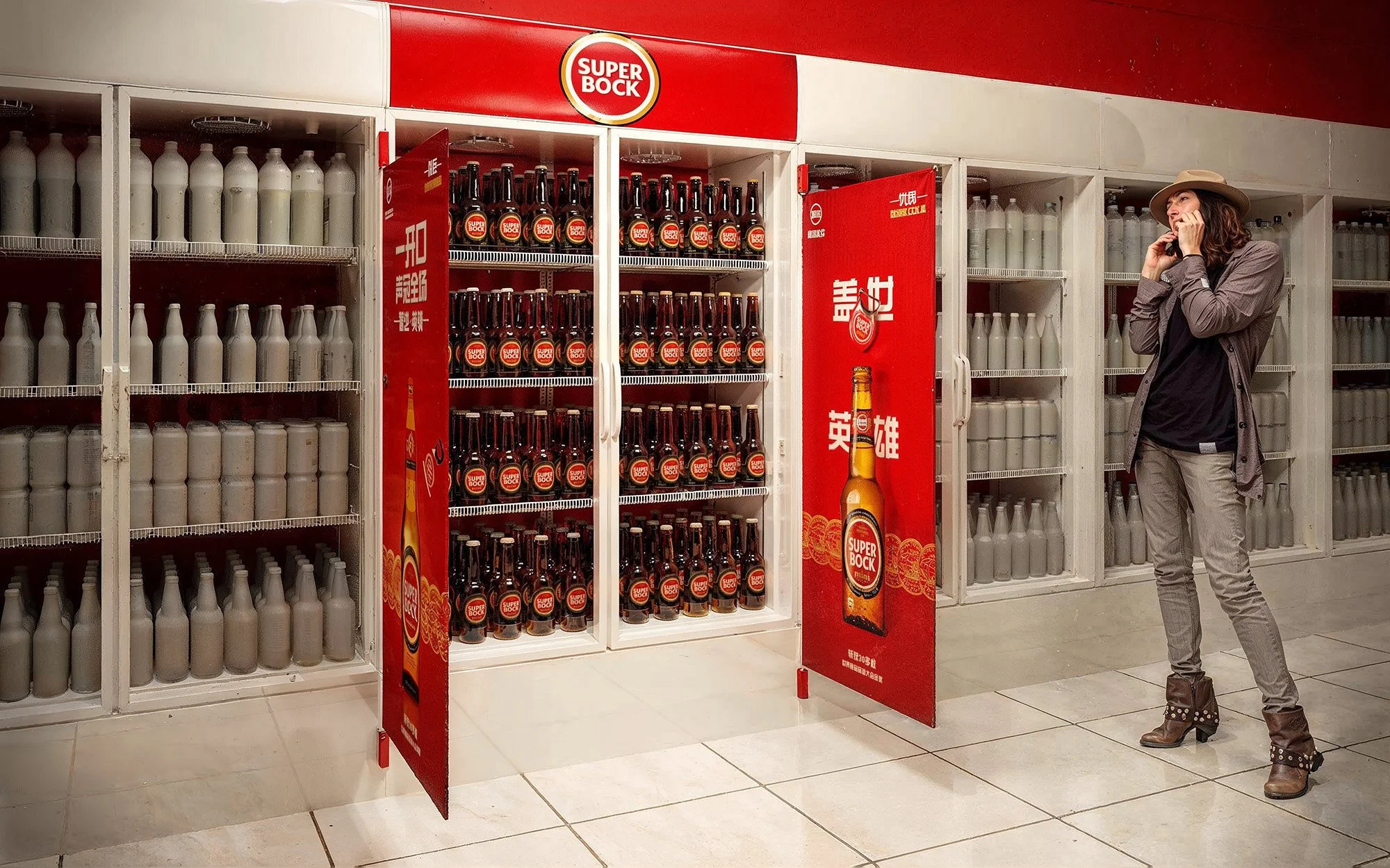 A woman stands by a display of Super Bock beer bottles in a store, talking on her phone.