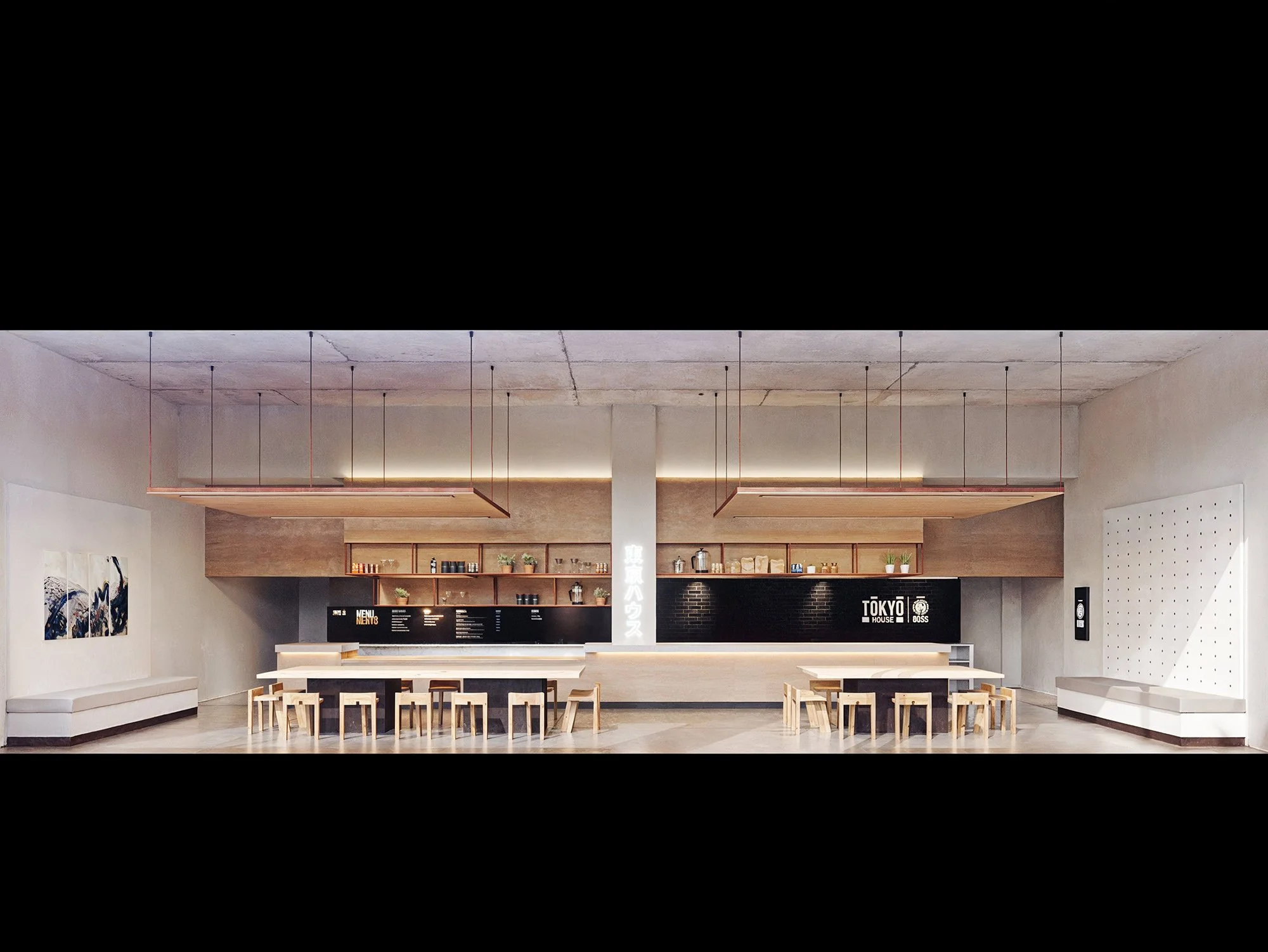 Modern minimalist interior of a café with a long counter, black menu boards, wooden shelves, and seating areas with white benches and wooden chairs.