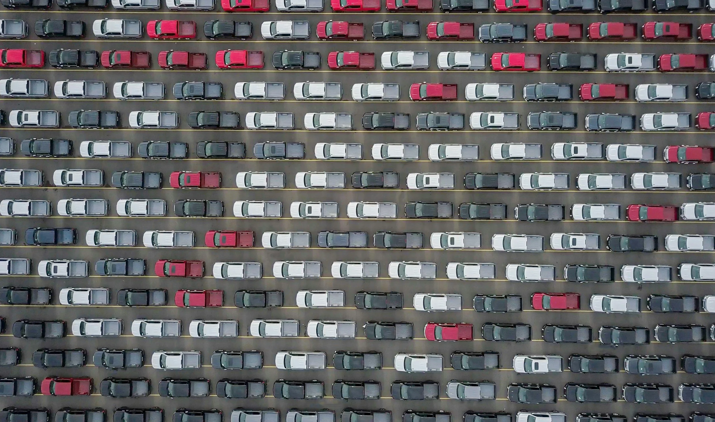 Overhead view of a parking lot filled with white, black, gray, and red cars parked in organized rows.