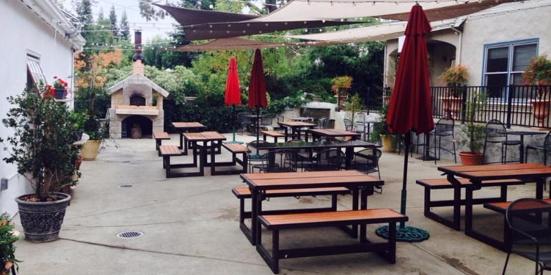 Patio seating with picnic tables, umbrellas, and a pizza oven at Farmhaus Restaurant