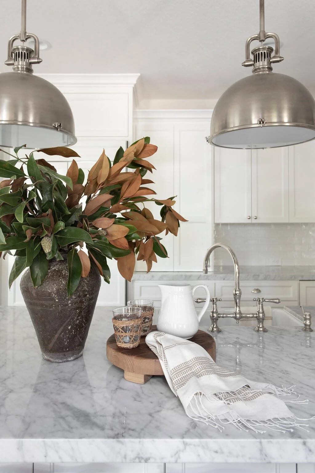 A close up of a marble kitchen countertop with a pitcher, water glasses, and a beautiful potted plant
