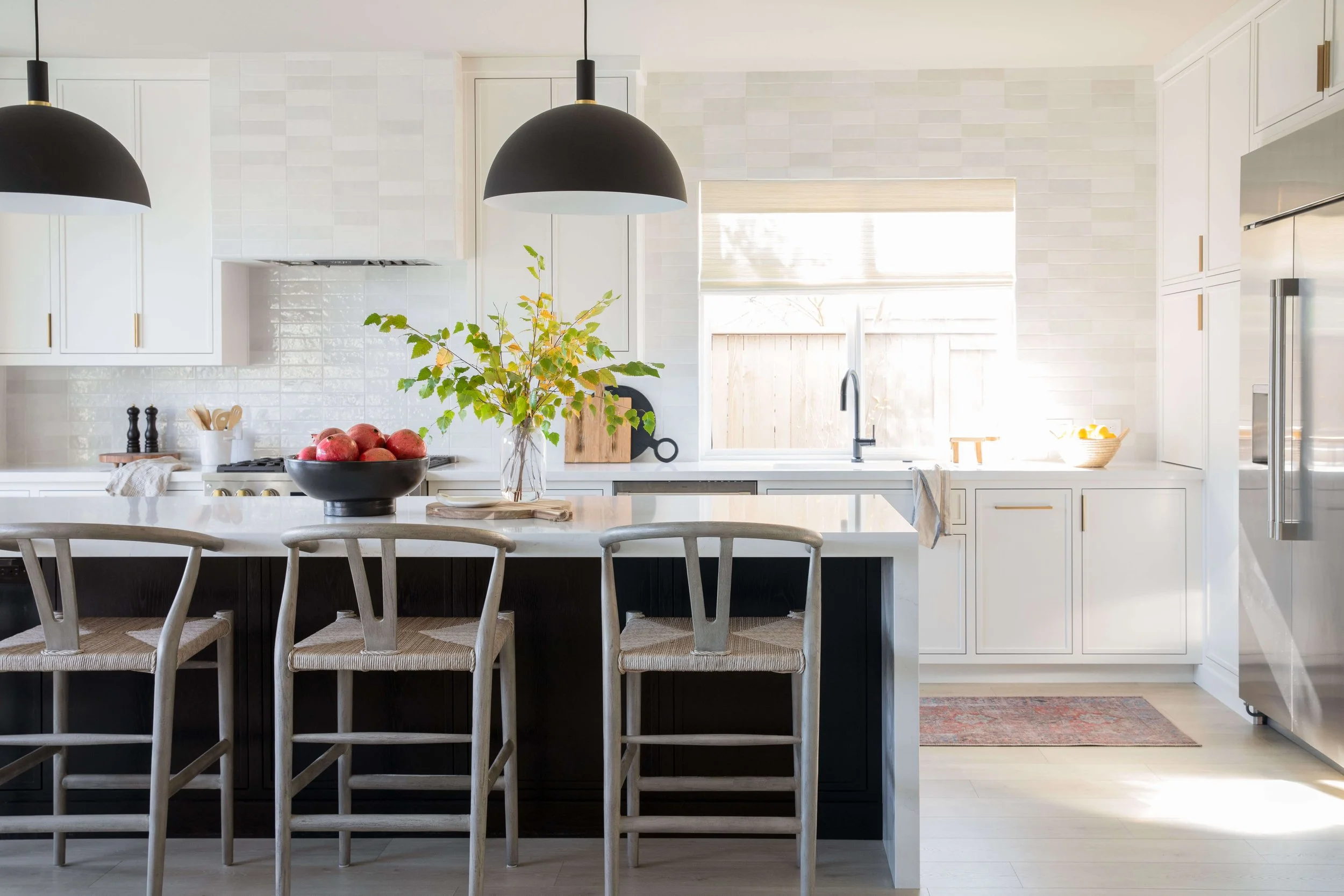 Bright kitchen with tile backsplash, white cabinetry, and black island lighting