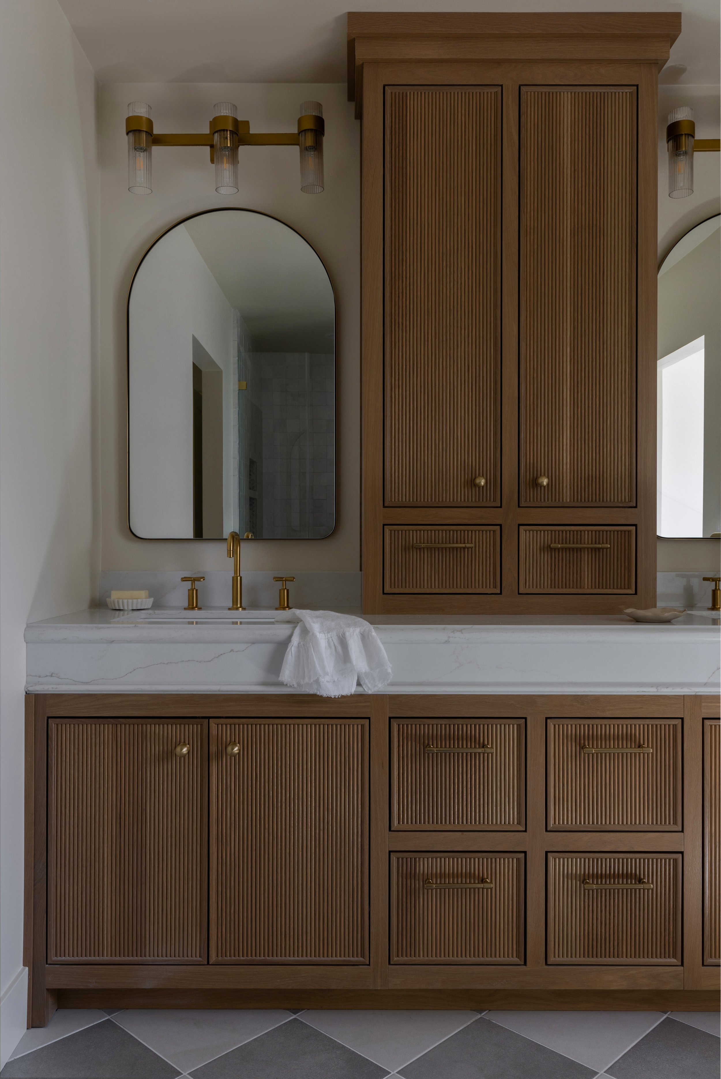 Bathroom vanity with wooden cabinets, a marble countertop, gold fixtures, a large mirror, and a white towel hanging over the sink.