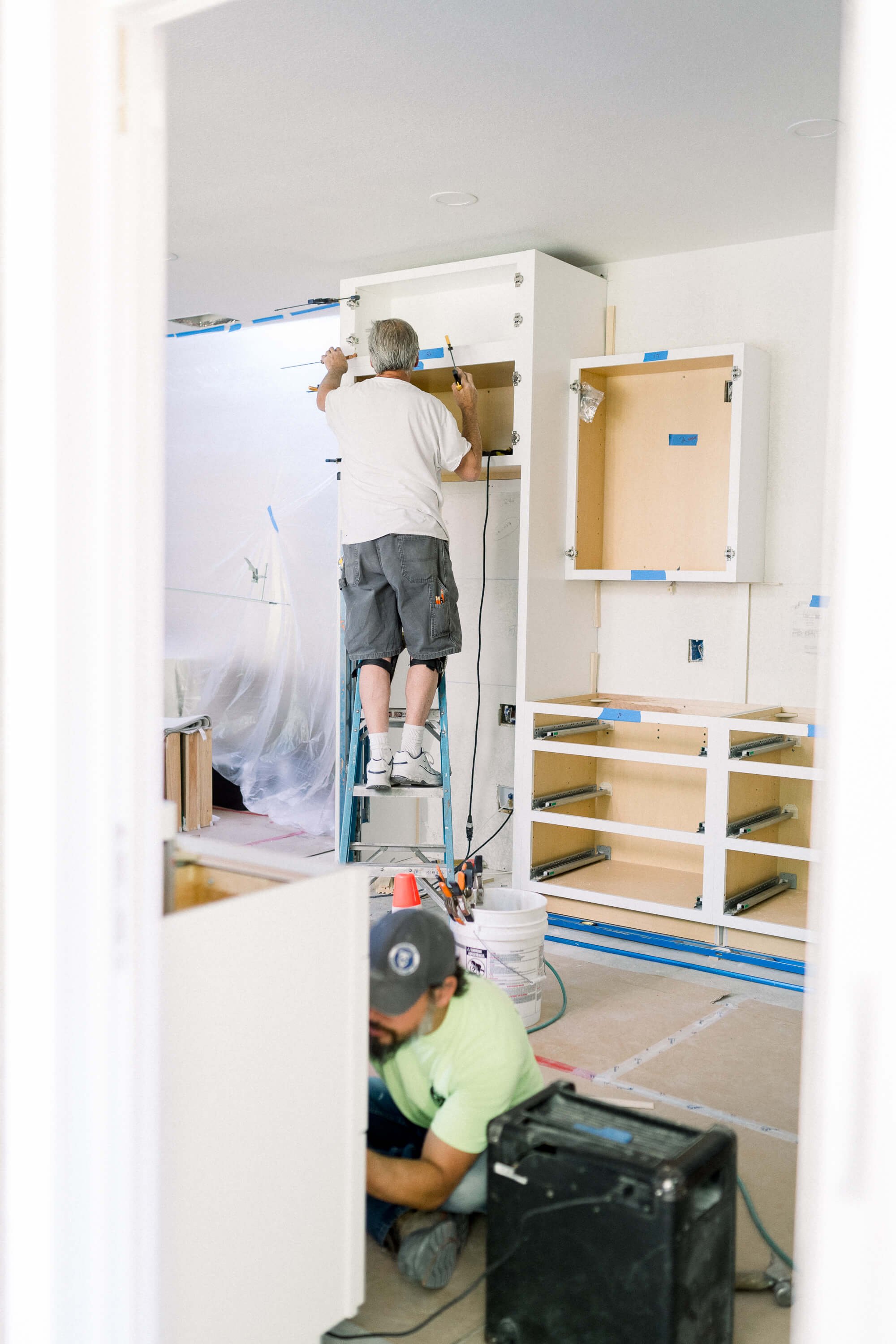 A man on a ladder installing cabinetry