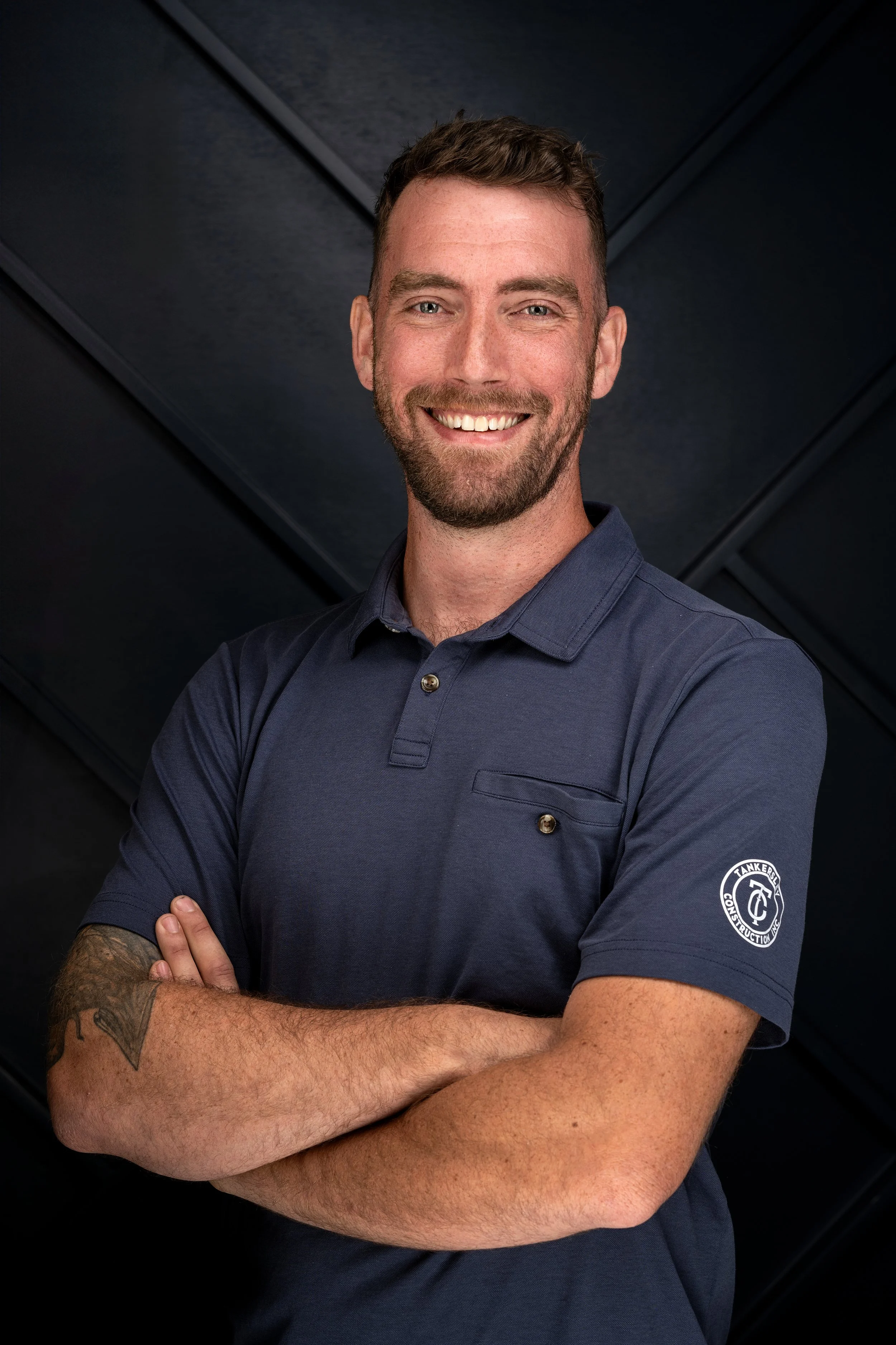 A smiling Tankersley Build Co Employee headshot. He is standing against a dark, textured background.