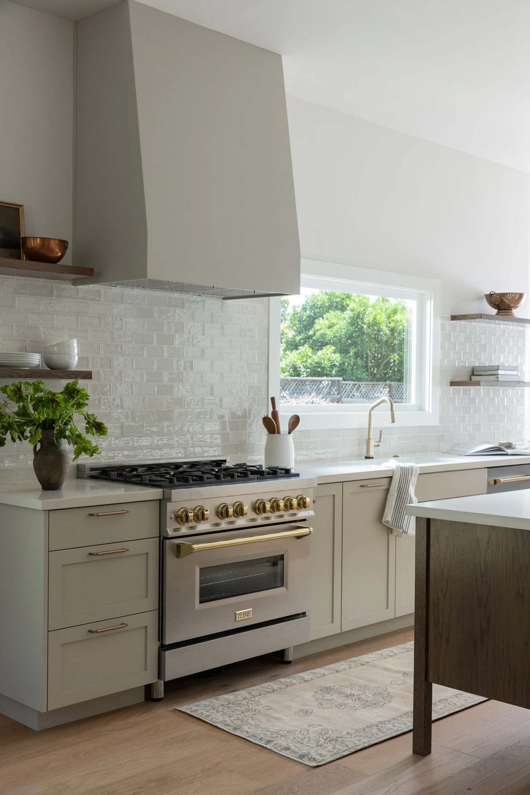 Custom designed kitchen with white cabinets, a stainless steel oven, open shelving, green plant, and window with natural light.