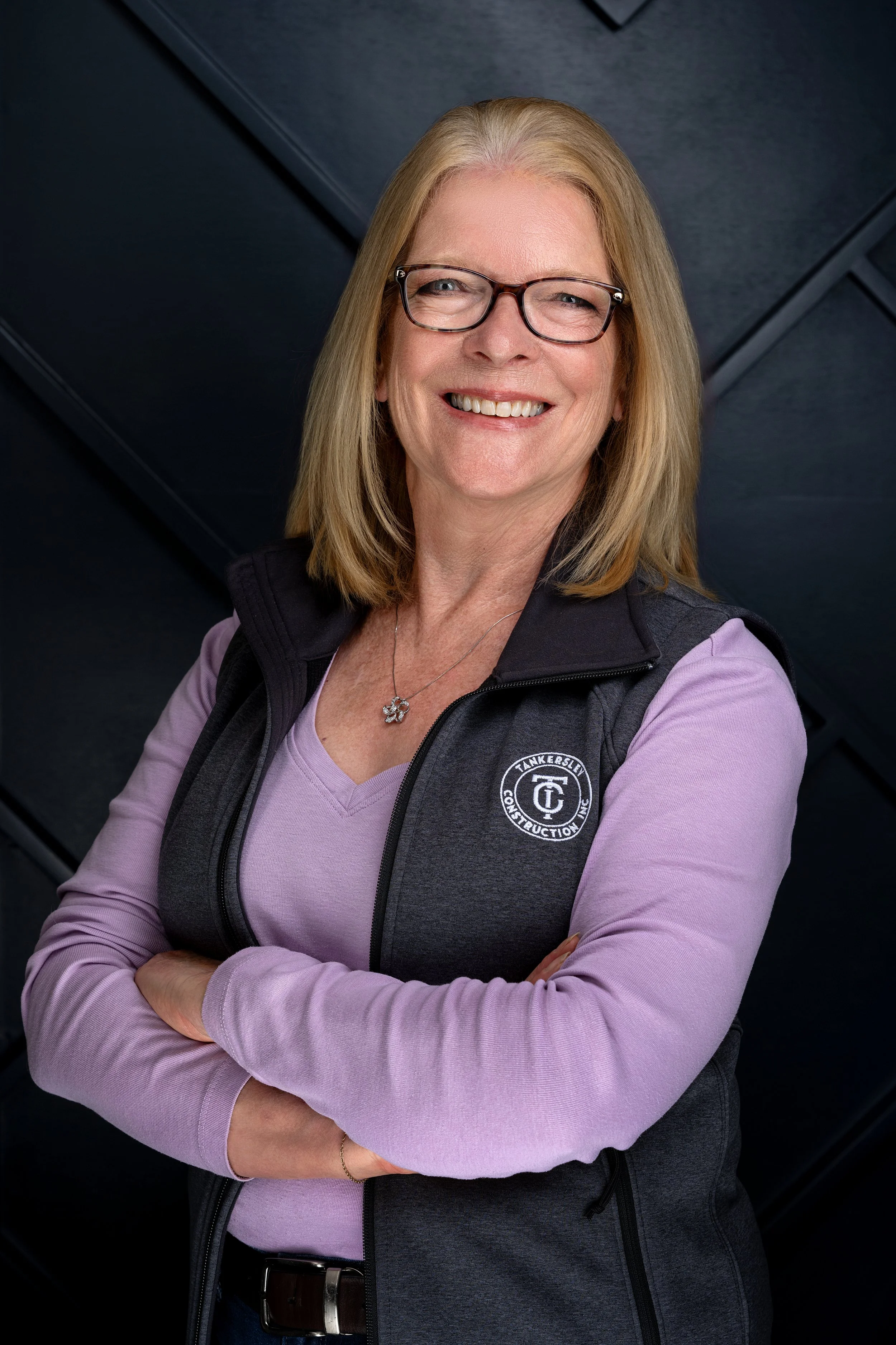 A portrait of a Tankersley Build Co Employee headshot. She is standing against a dark, textured background.