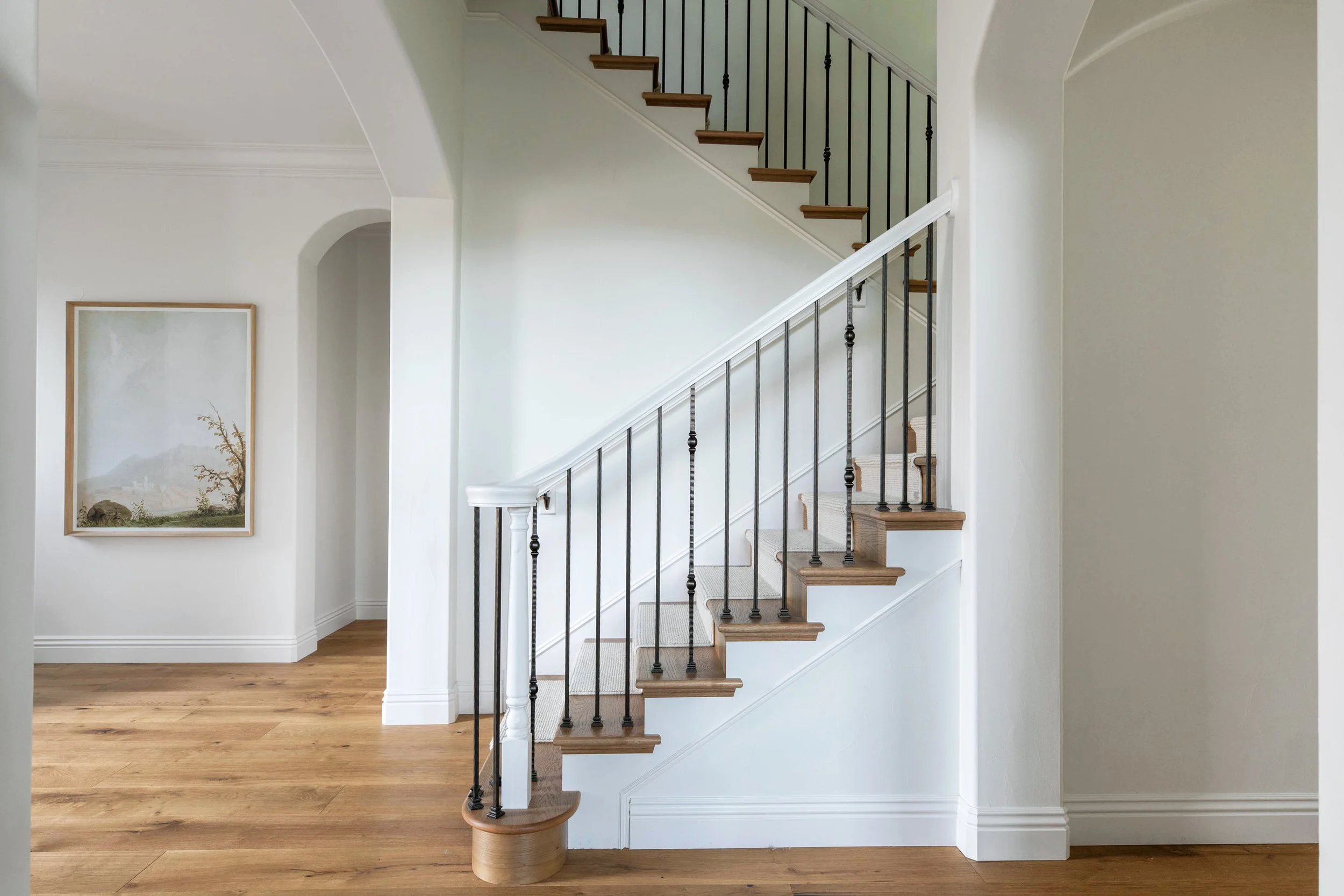 Interior view of a house showing a staircase with wooden steps, black metal balusters, and a white handrail.