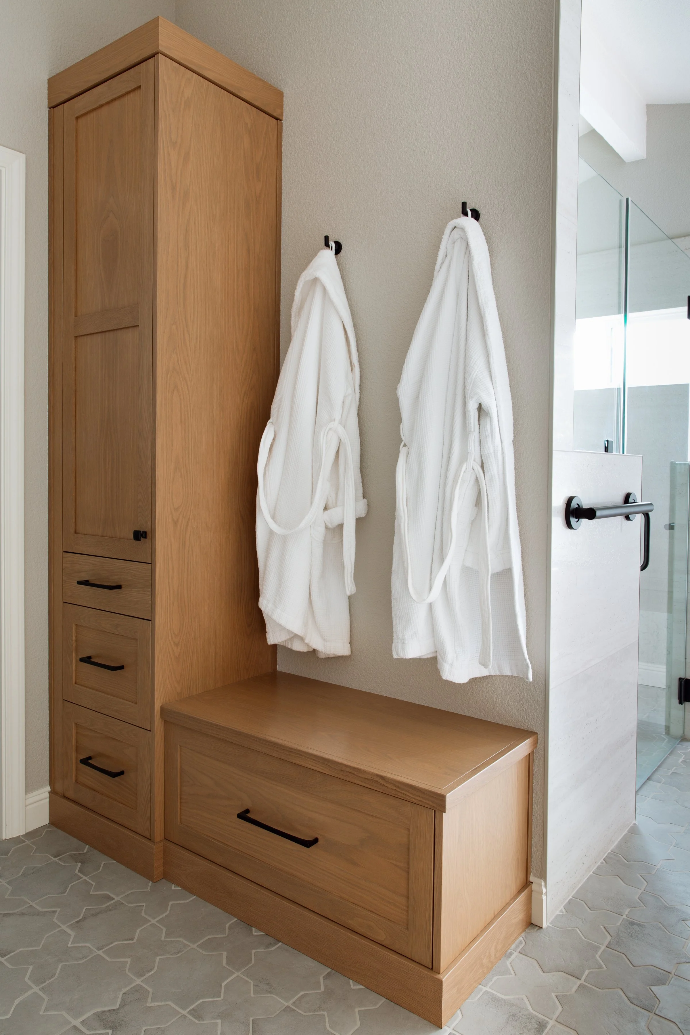 Two robes hang next to built-in cabinetry and a walk-in shower in this Folsom aging-in-place remodel