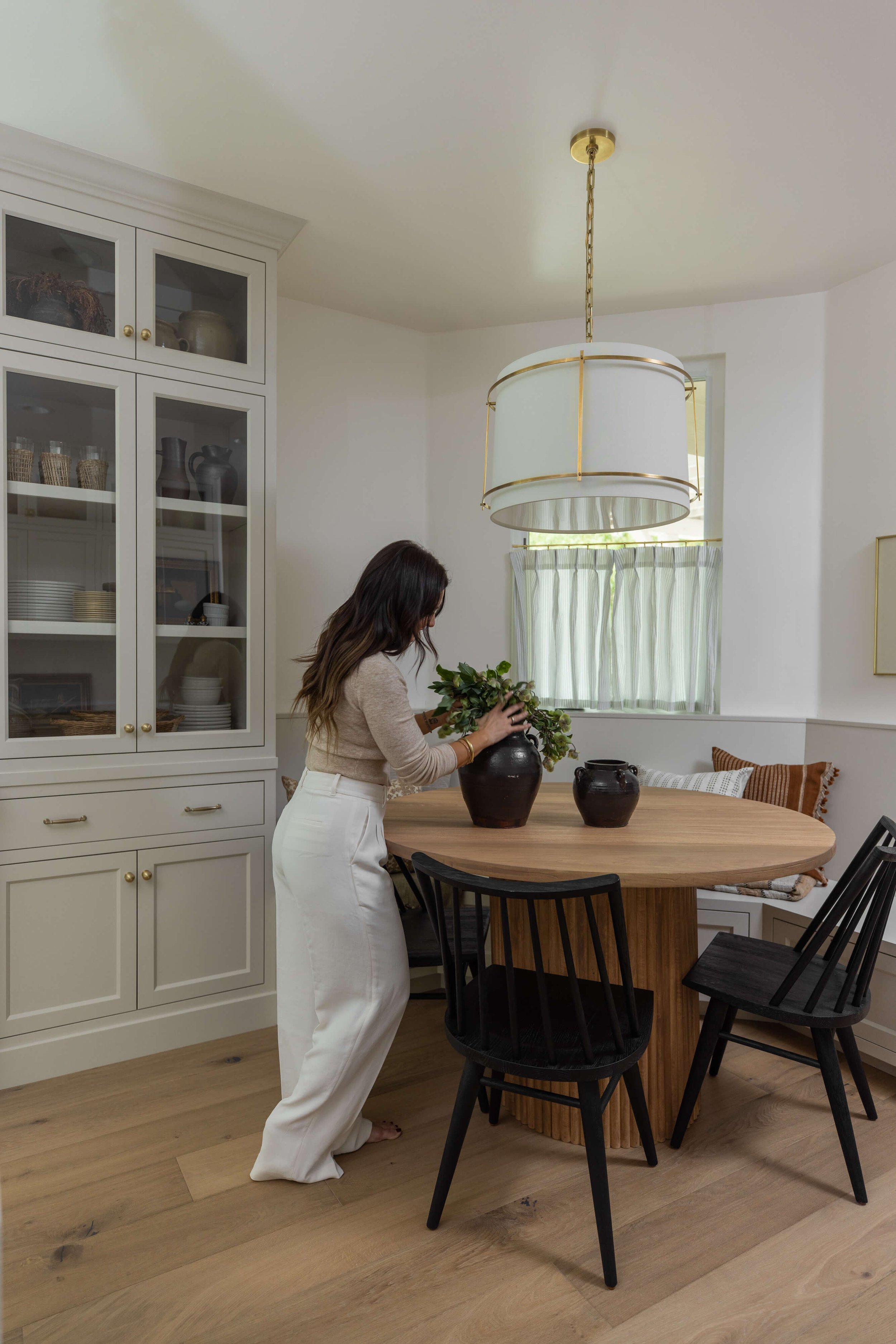 An interior designer prepares a plant in a vase on a kitchen table