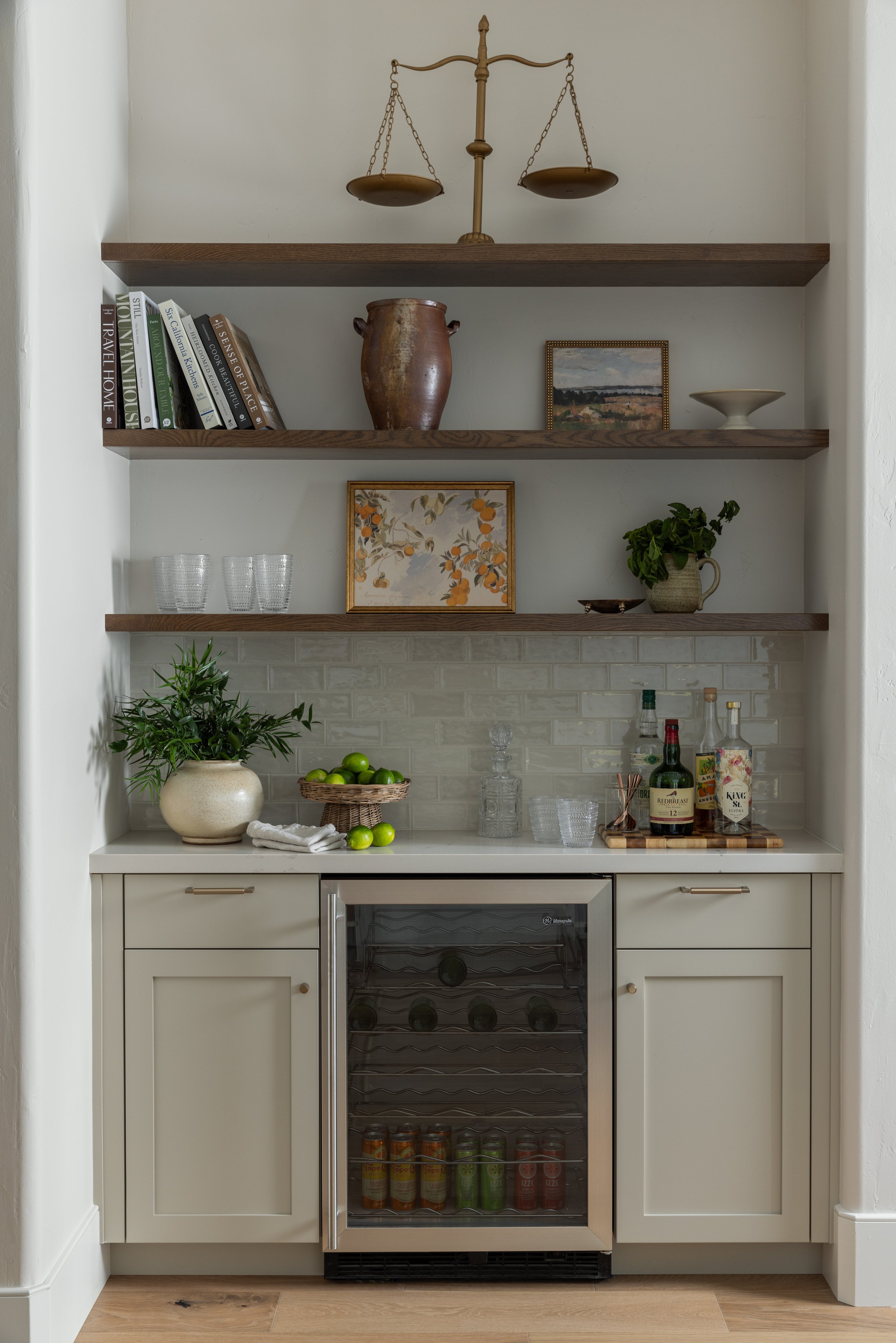 Built-in bar area with open wooden shelves, decorative objects, books, plants, and a mini wine cooler.