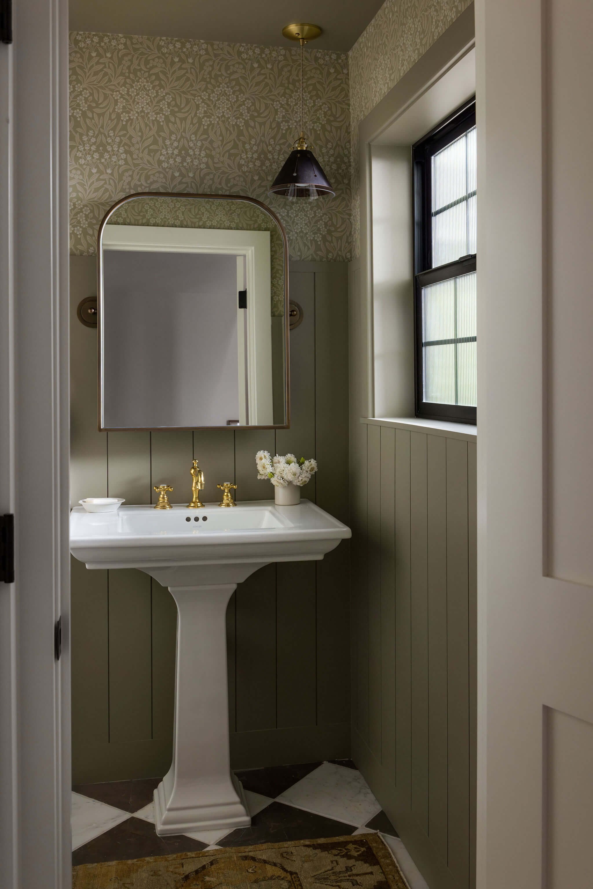 Looking into a powder bathroom with gray green walls and gold accents