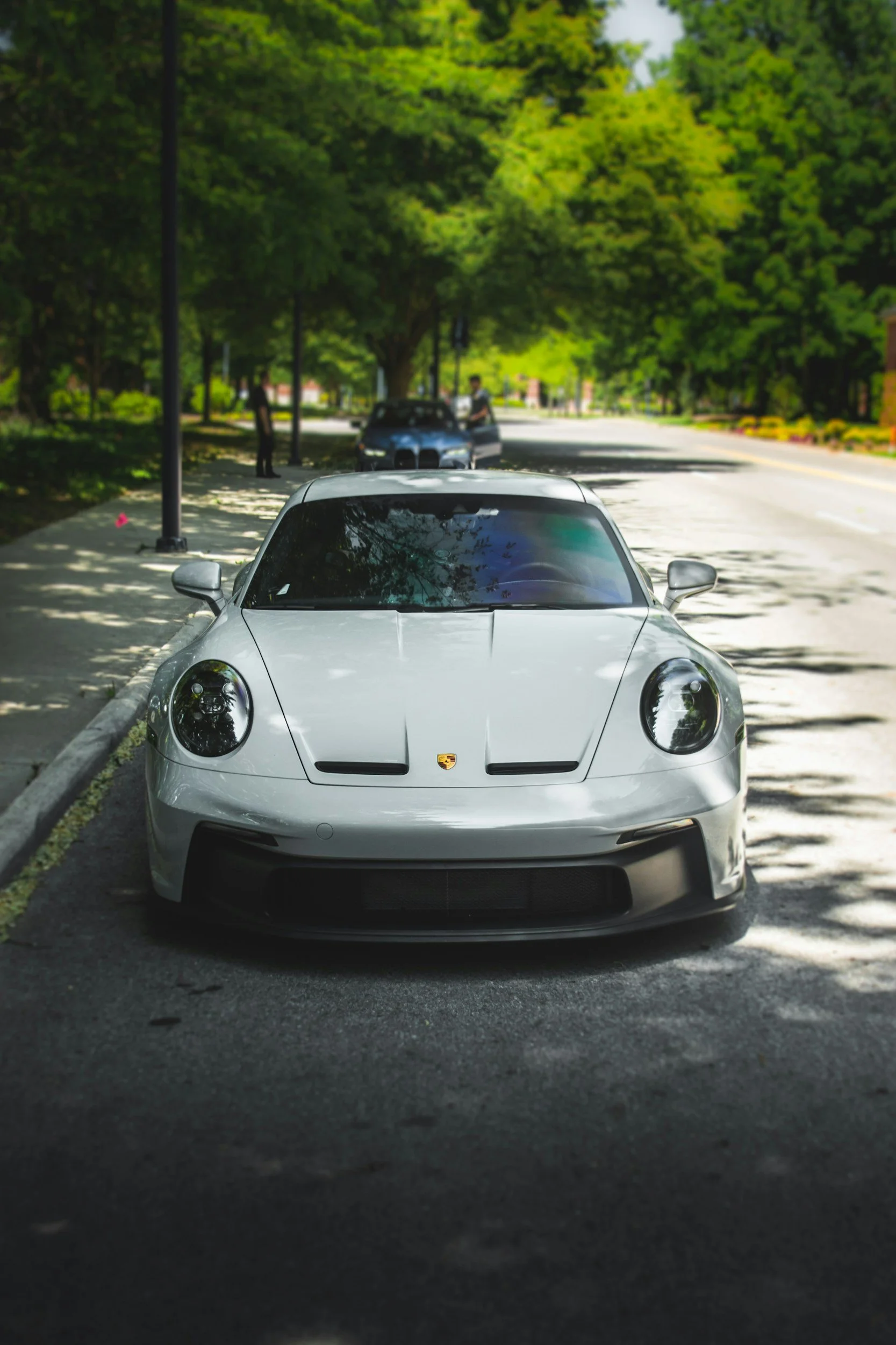 White Porsche sports car parked on the side of a tree-lined street in daytime.