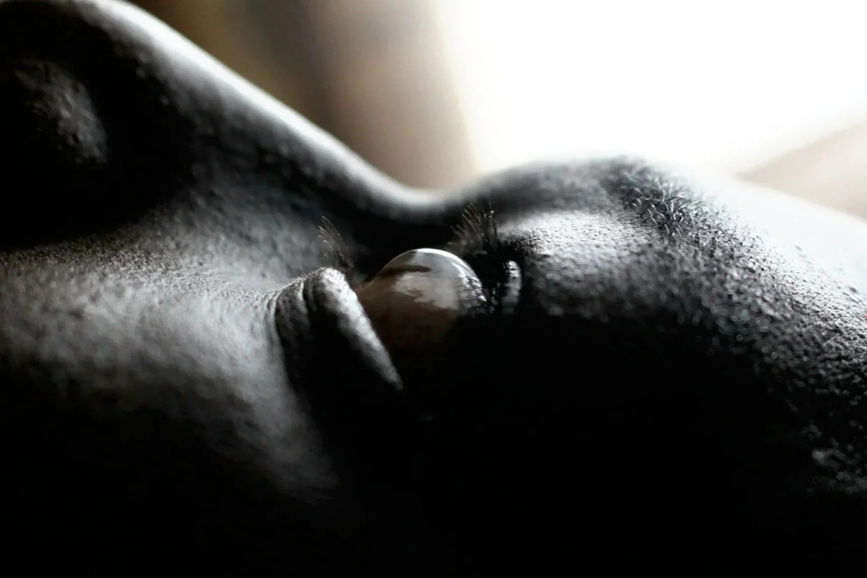 Close-up of a person's face with shiny eye, and textured skin, in soft lighting.