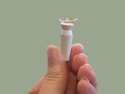 A hand holding a small medical device with a metal tip against a solid light green background.