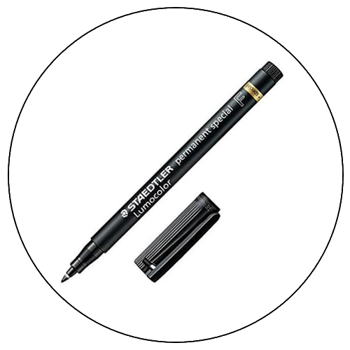 A black STAEDTLER Lumocolor permanent marker with its cap removed, lying on a white circular surface.