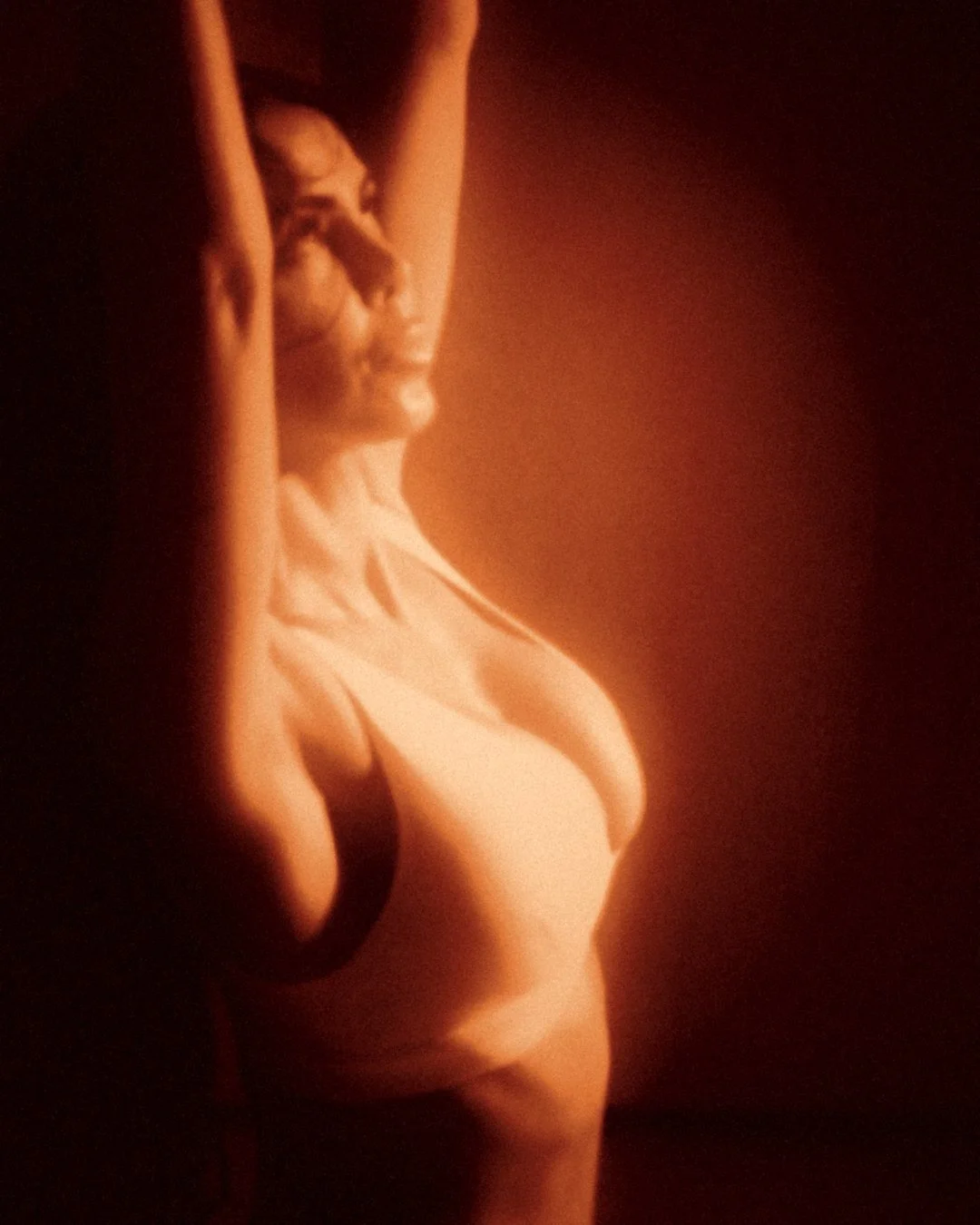 Arms overhead, glowing in a pool of amber light