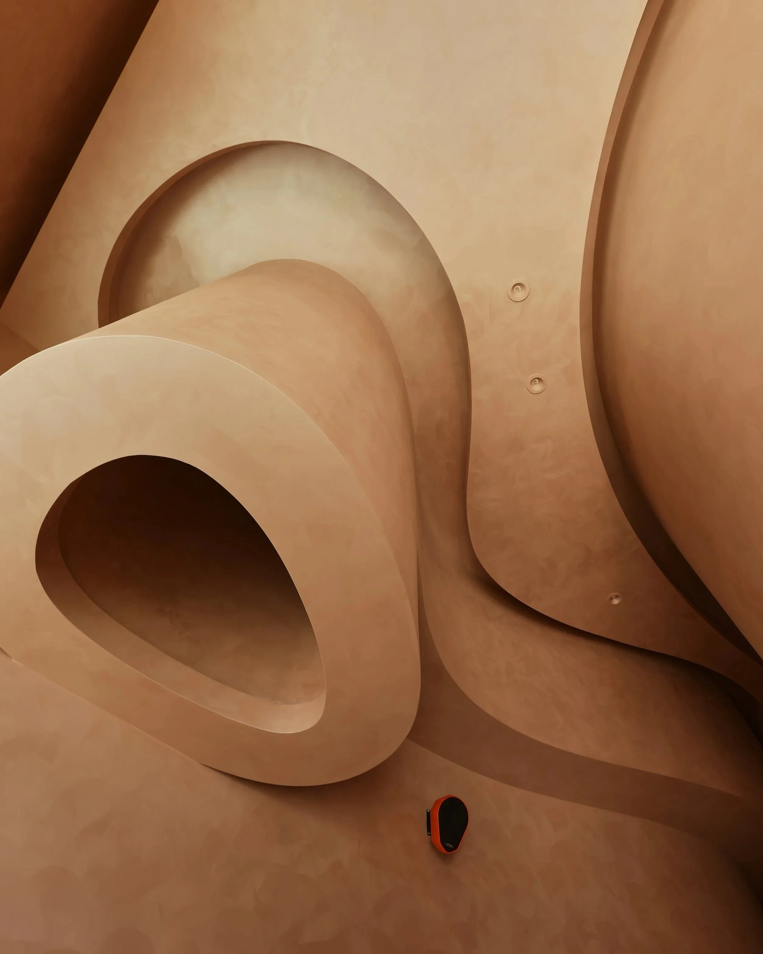 Abstract architectural ceiling with large curved and rounded shapes in beige and cream tones, and a small orange & black VOID Acoustics speaker.