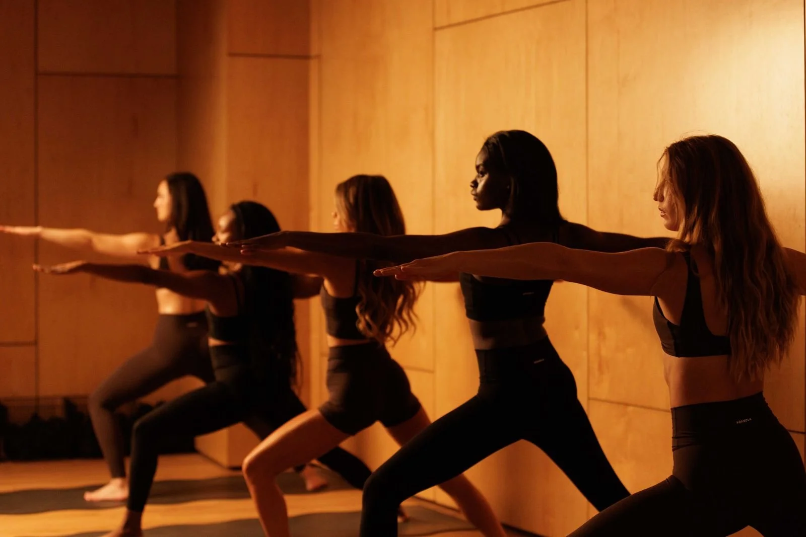 Flow Sculpt: a row of women holding warrior two in amber light