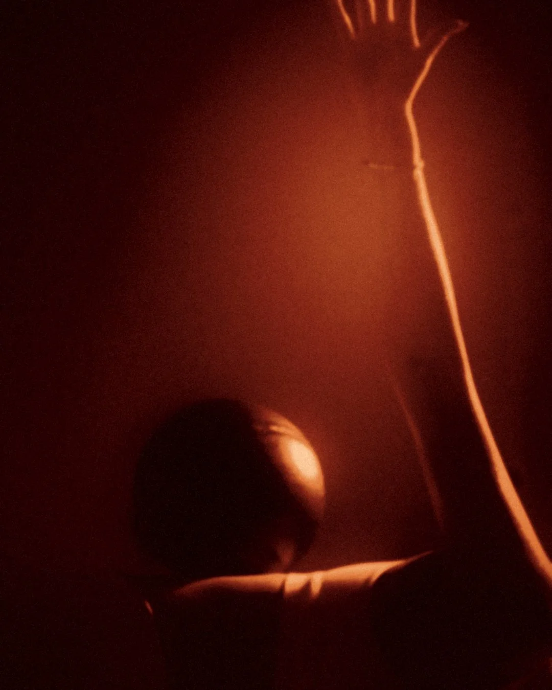 Pilates Burn: one arm reaching high, a ball in hand, in amber light