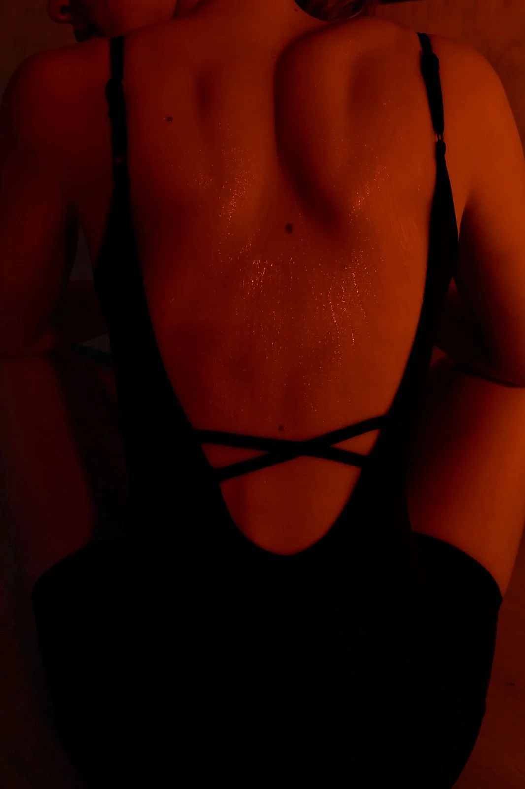 A sweat-slick back in a strappy black set, warm red light