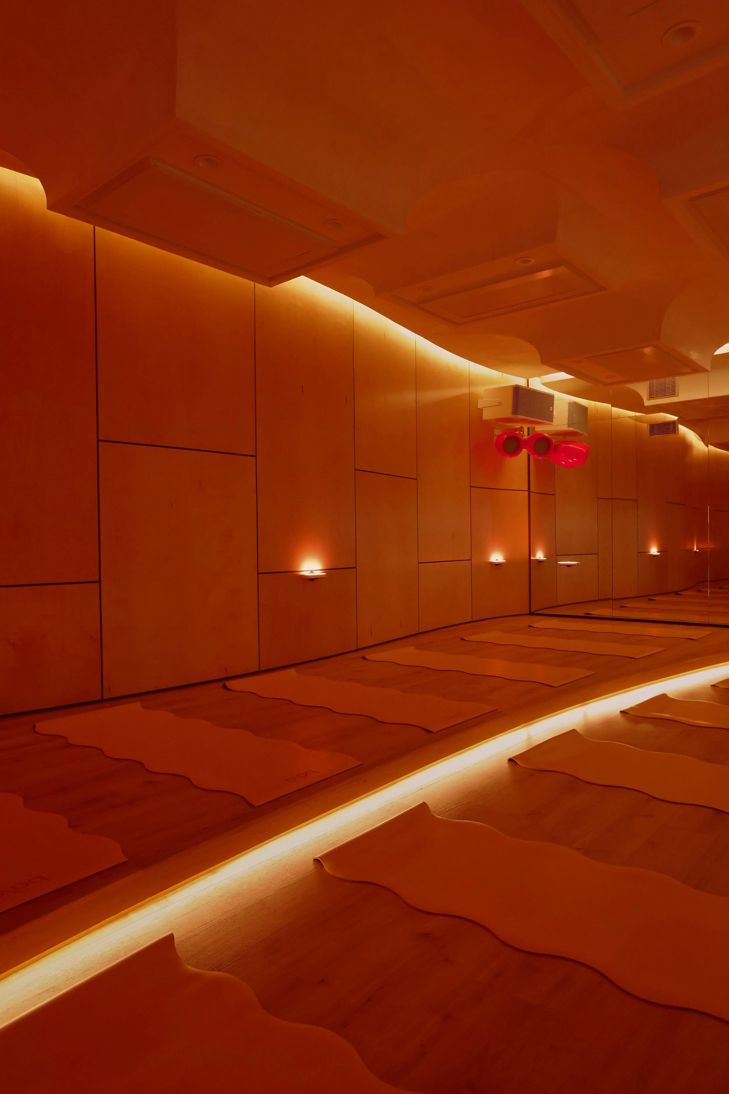 A dimly lit yoga studio with wooden walls, mats on the floor, and red lighting on the wall.